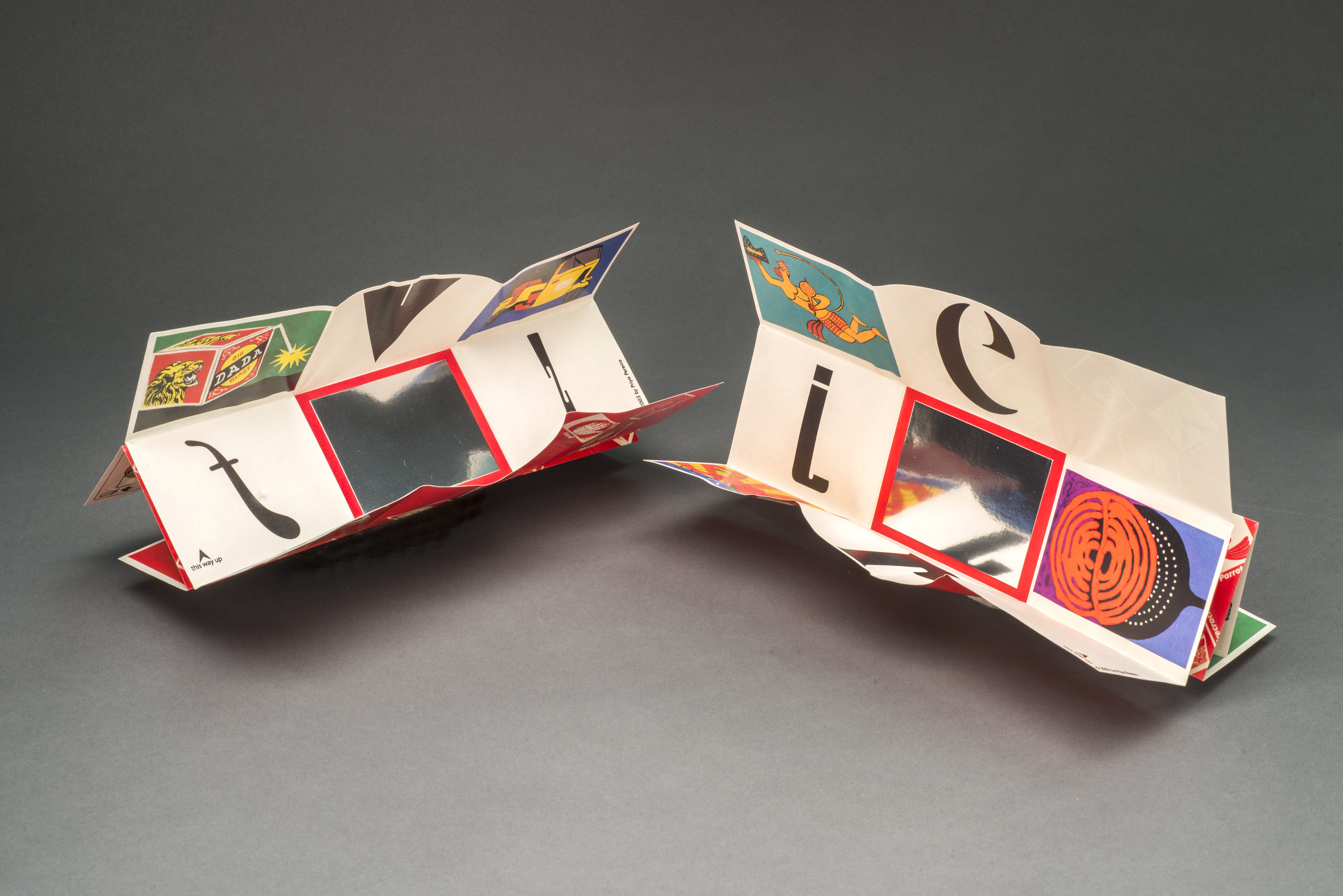 Two artists books with intricate folds and colorful panels sit side-by-side.