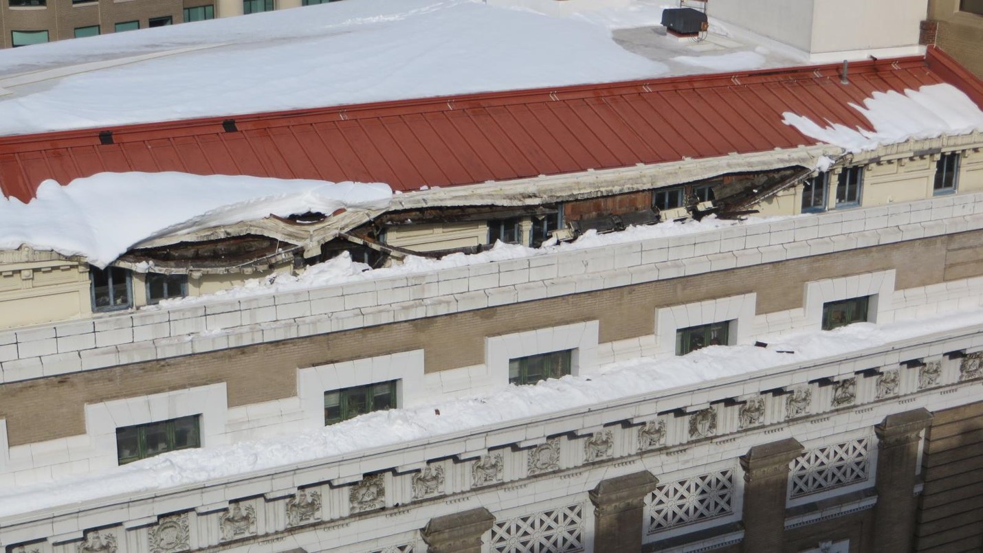 Close-up of museum's exterior roof showing damage to the gutters caused by heavy snow that is also present in the photograph.