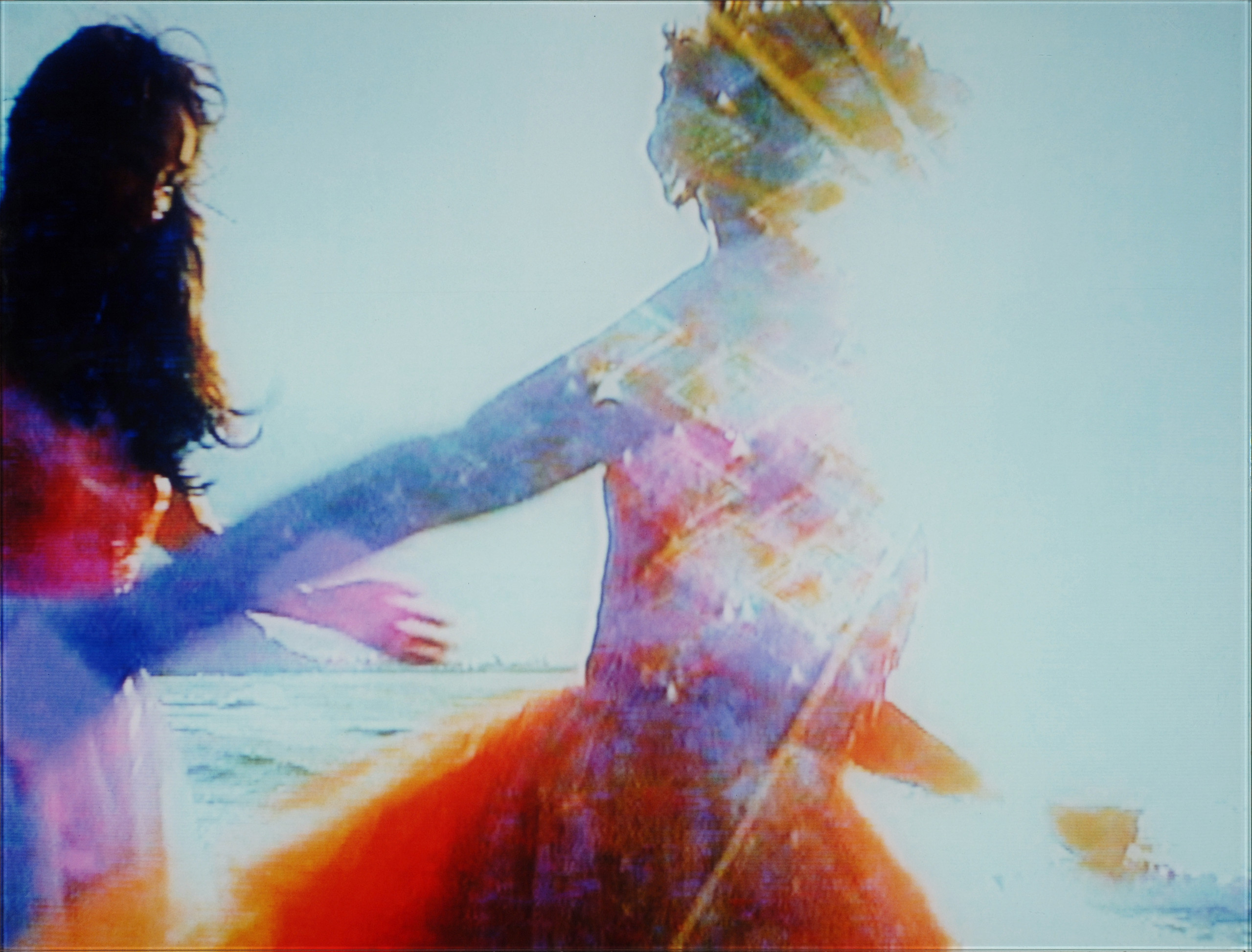 A screen still of a video that features the figures of two women, one with short blonde hair, one with long brown hair, in motion. They are slightly pixelated/abstract. The contrast is high and particulars of the image are washed out. There is perhaps an oceanside mountain and the sea in the background.