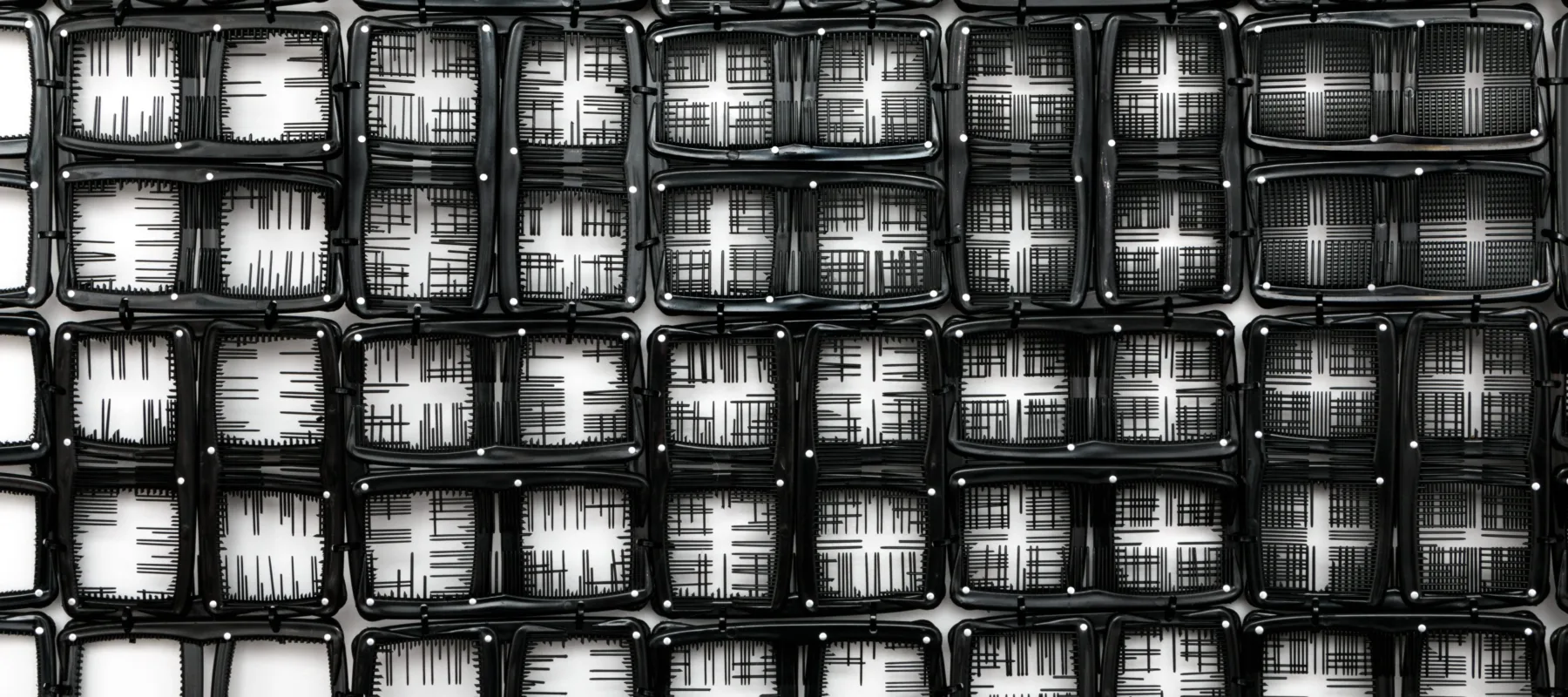 A detail photograph of black pocket combs arranged into a gride of squares. In some squares, the teeth have been snipped so the background is white, in others select teeth are left creating fine black lines. Still in others squares, the majority of teeth have been left creating a predominately black background.