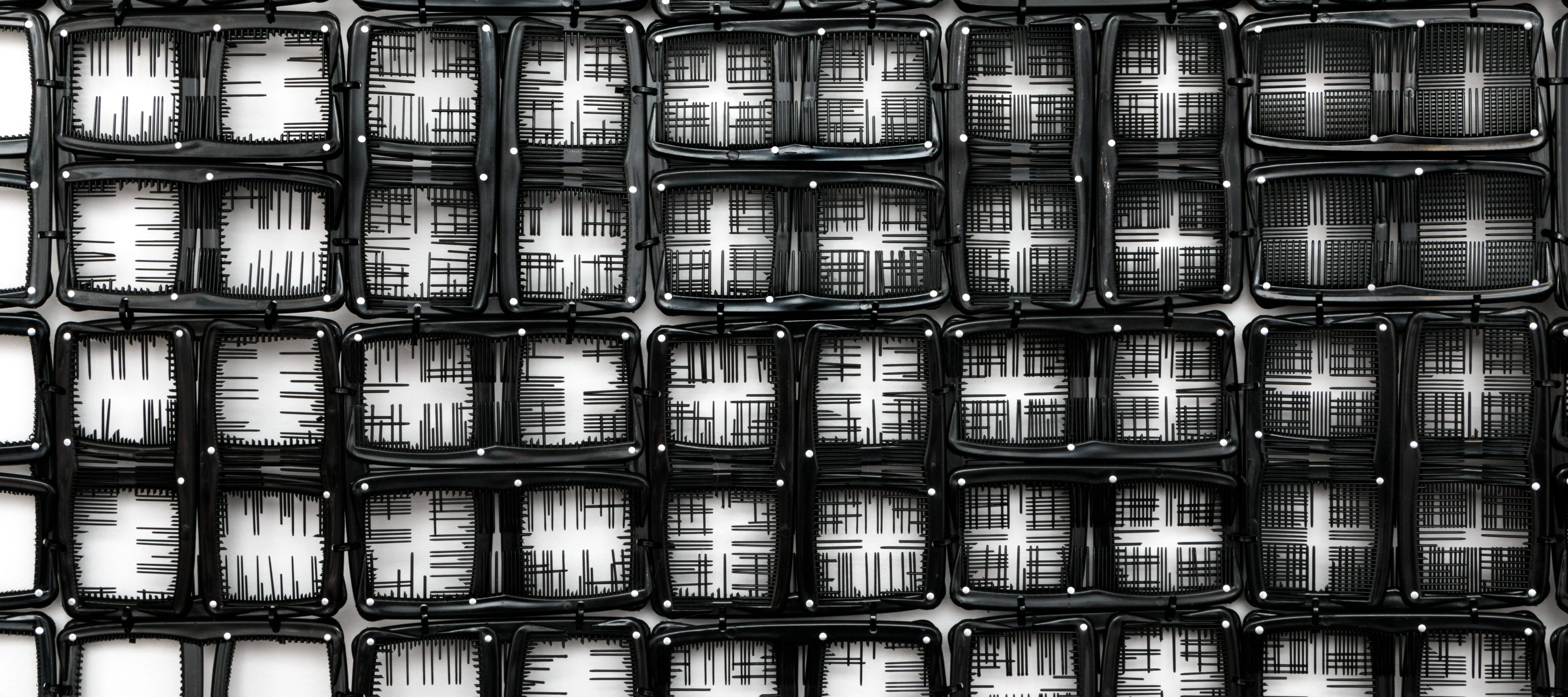 A detail photograph of black pocket combs arranged into a gride of squares. In some squares, the teeth have been snipped so the background is white, in others select teeth are left creating fine black lines. Still in others squares, the majority of teeth have been left creating a predominately black background.