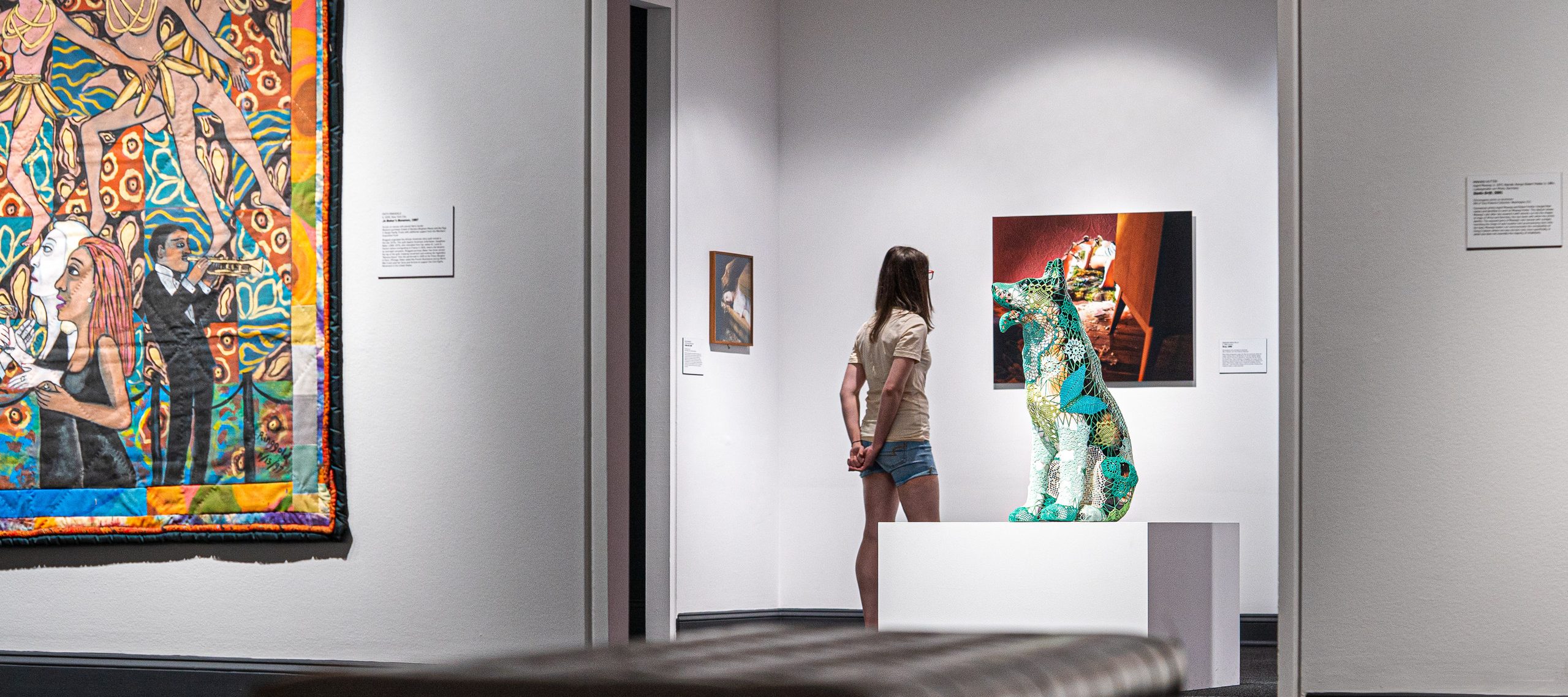 A young woman with light skin walks through the galleries with her hands clasped behind her back.