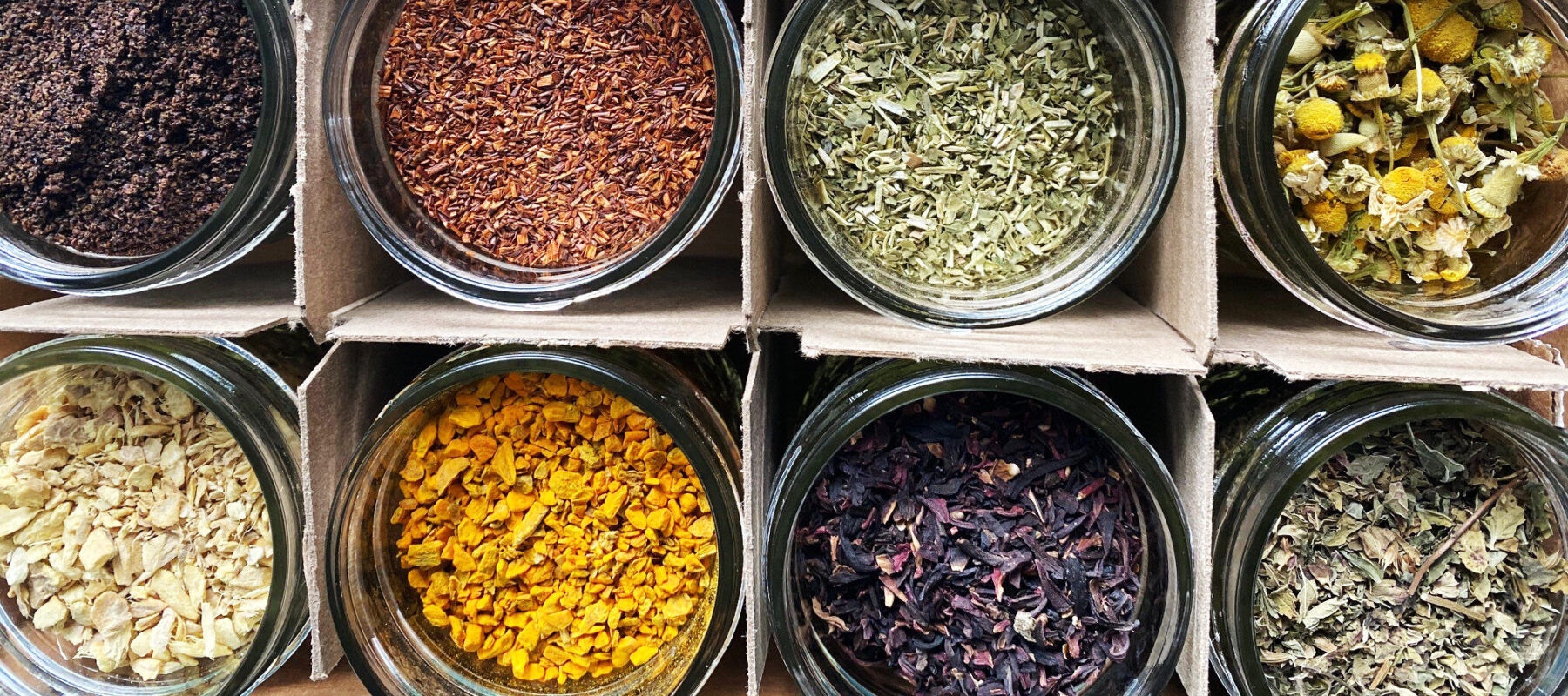 An arial view of round jars full of colorful spices, arranged in a four by three cardboard grid.