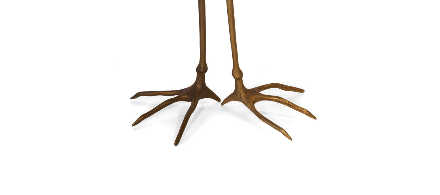 Surrealist sculpture and functional occasional table is shown from above at a high angle; the work features realistic cast bronze crane legs holding a round wooden, gold-plated tabletop.