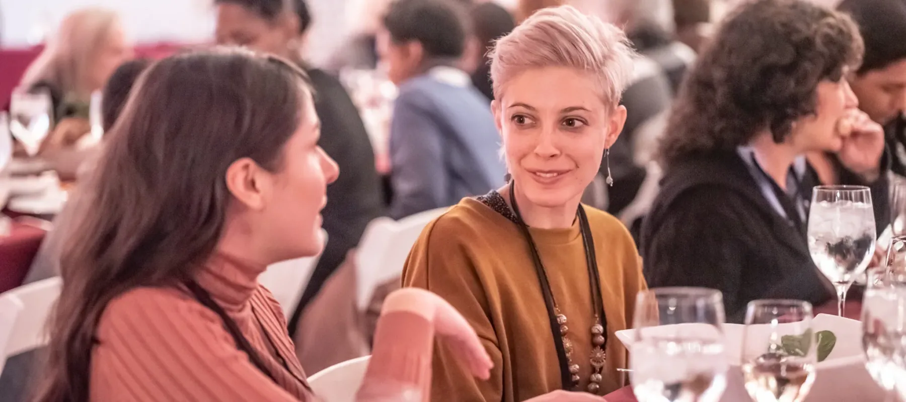 Two women have a conversation over plates of food.