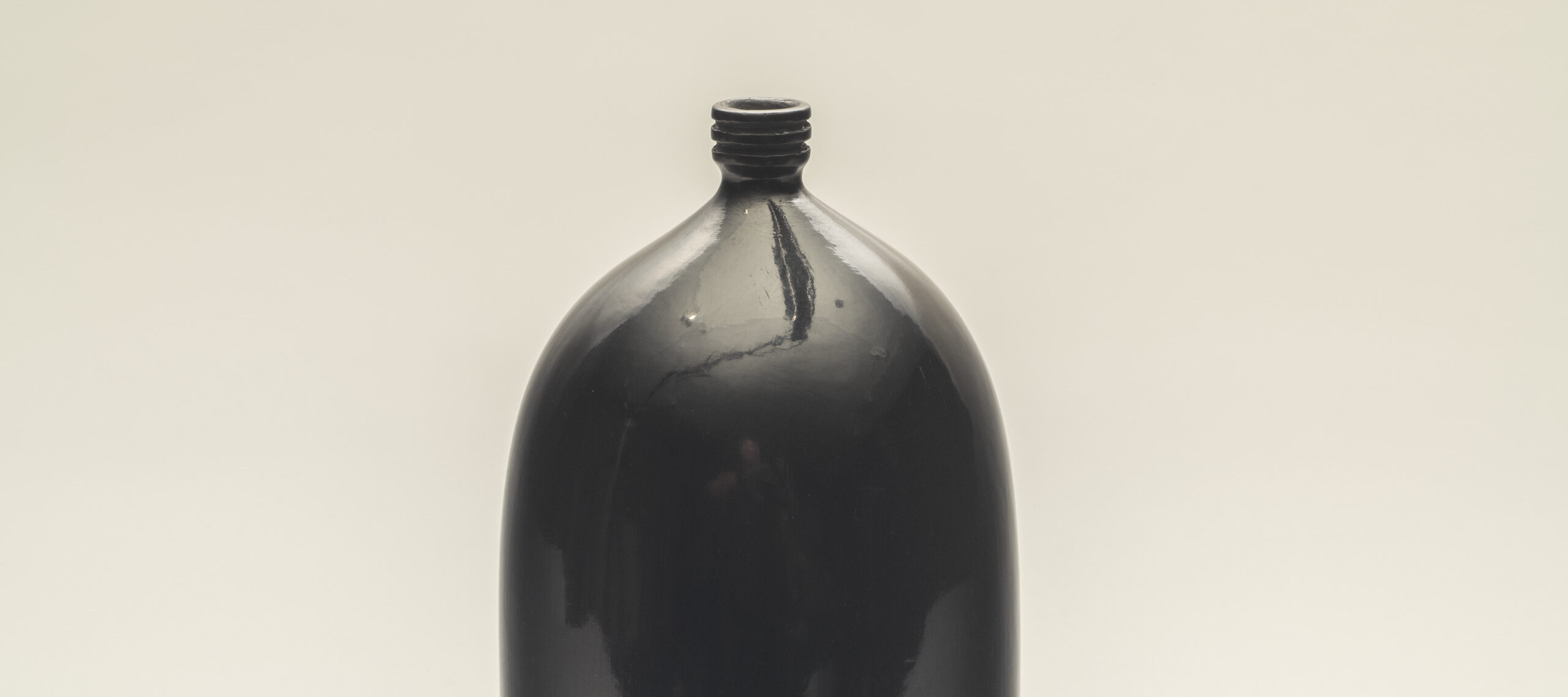 A smooth, glazed, black clay vessel shaped like a two-liter soda bottle.