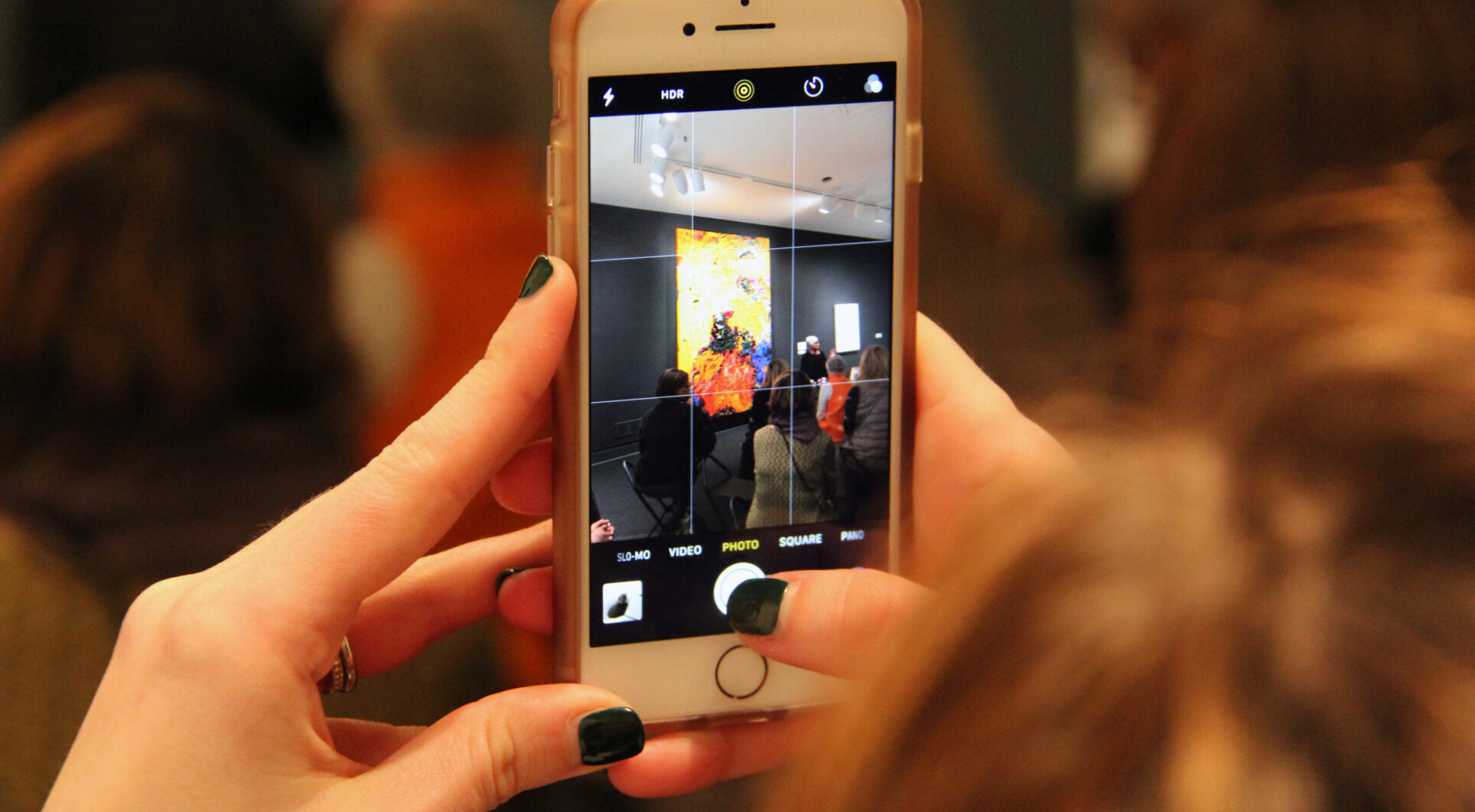 Close-up of hands holding a smartphone recording an artist talk in front of a yellow artwork in the museum.