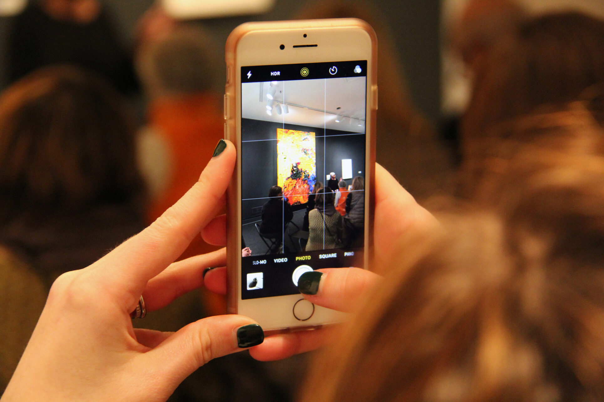 Close-up of hands holding a smartphone recording an artist talk in front of a yellow artwork in the museum.