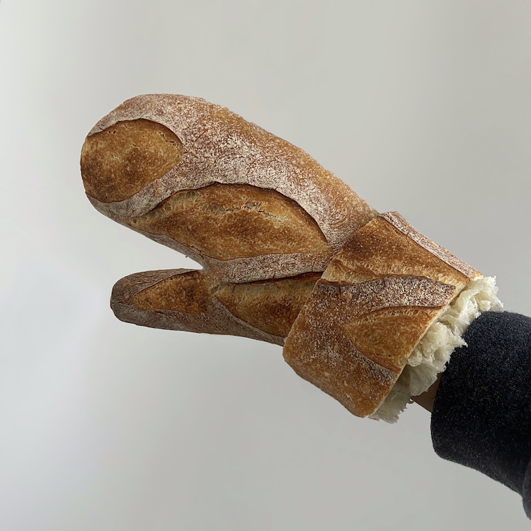 A photograph of a hand wearing a mitten. The mitten is made out of a loaf of rustic bread.