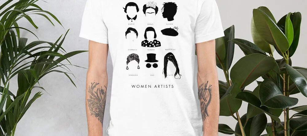 A light-skinned adult wears a white t-shirt that has a three by three array of nine illustrations featuring the iconic hair and accessories of famous women artists. Underneath each illustration is the artist’s name, and underneath the group are the words 'women artists.'