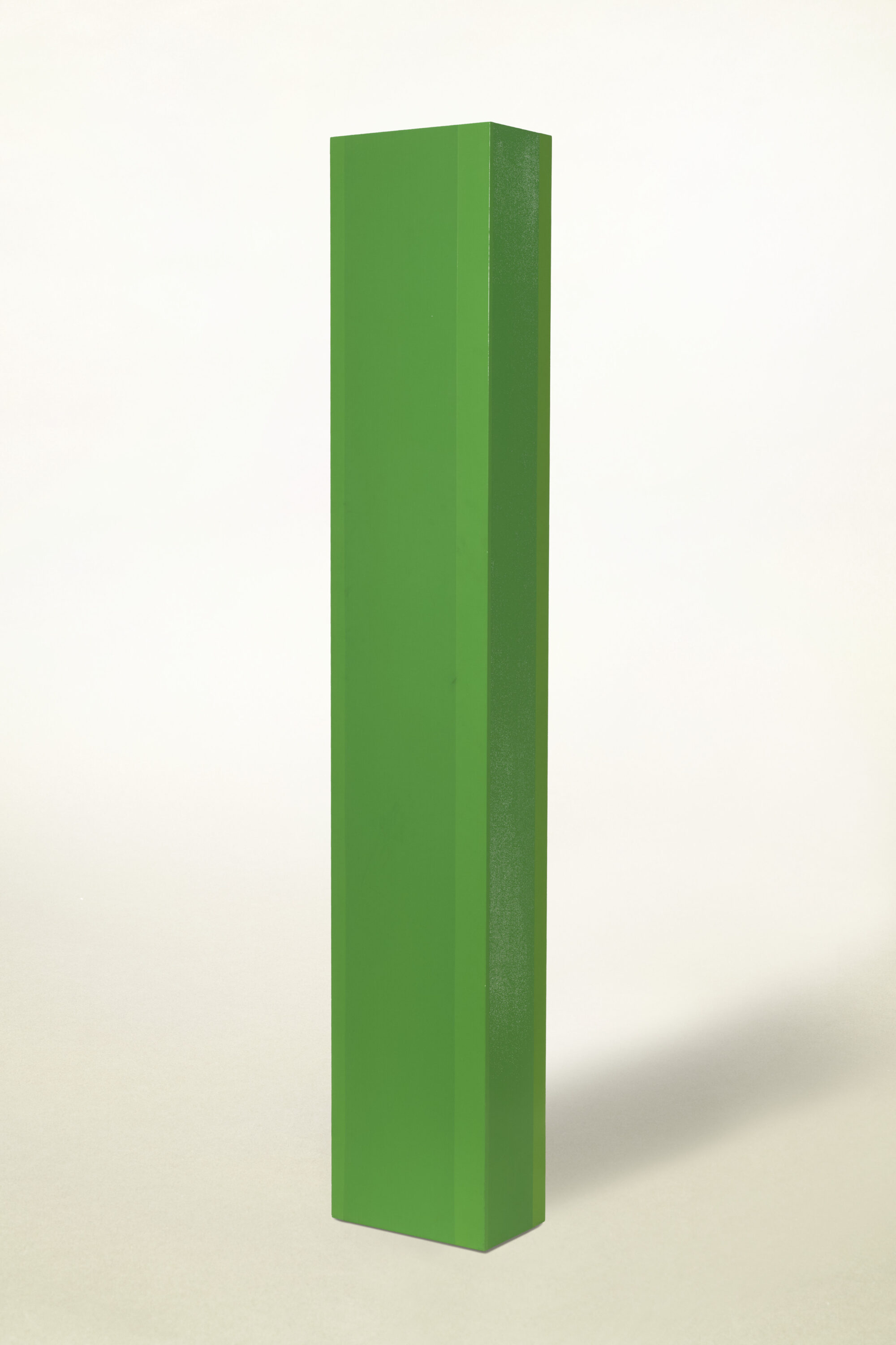 Tall, rectangular, pillar-like sculpture, painted in vibrant green hues on a smooth, clean surface. The sculpture stands against a solid white backdrop.