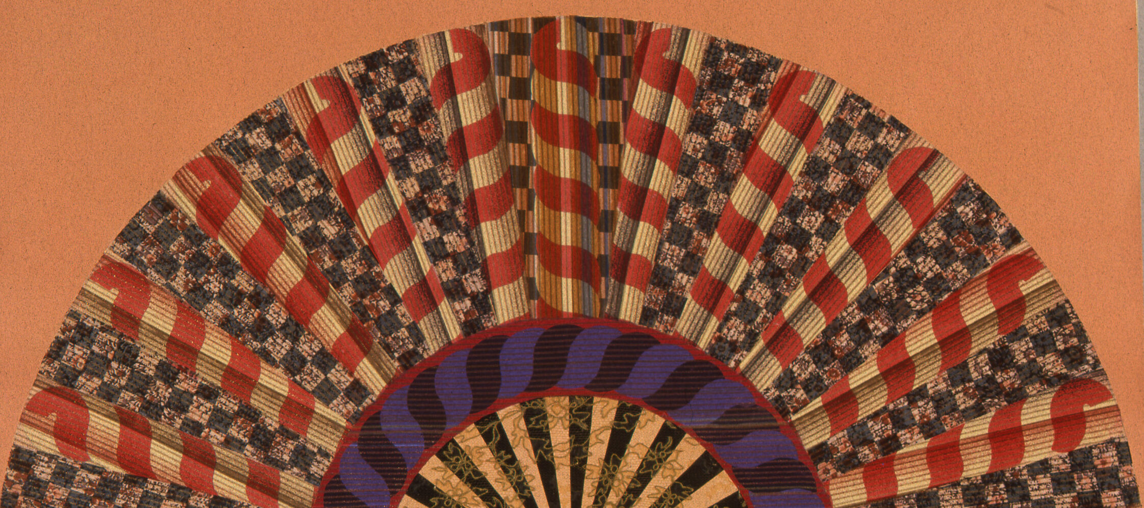 A colorfully painted and collaged folding fan spread open on a peach-orange background.