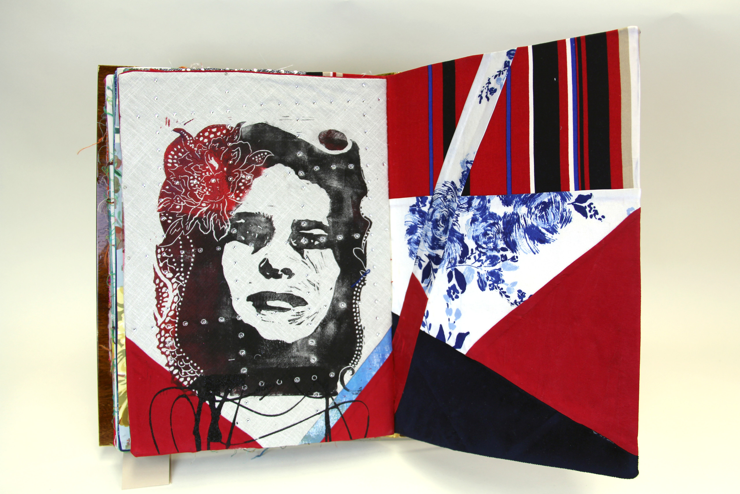 A book made from colorful print fabrics collaged and stitched together is laid flat and open to a spread that features an stencil cut image of a woman's face overlaid with an intricate flower positioned on her hair.