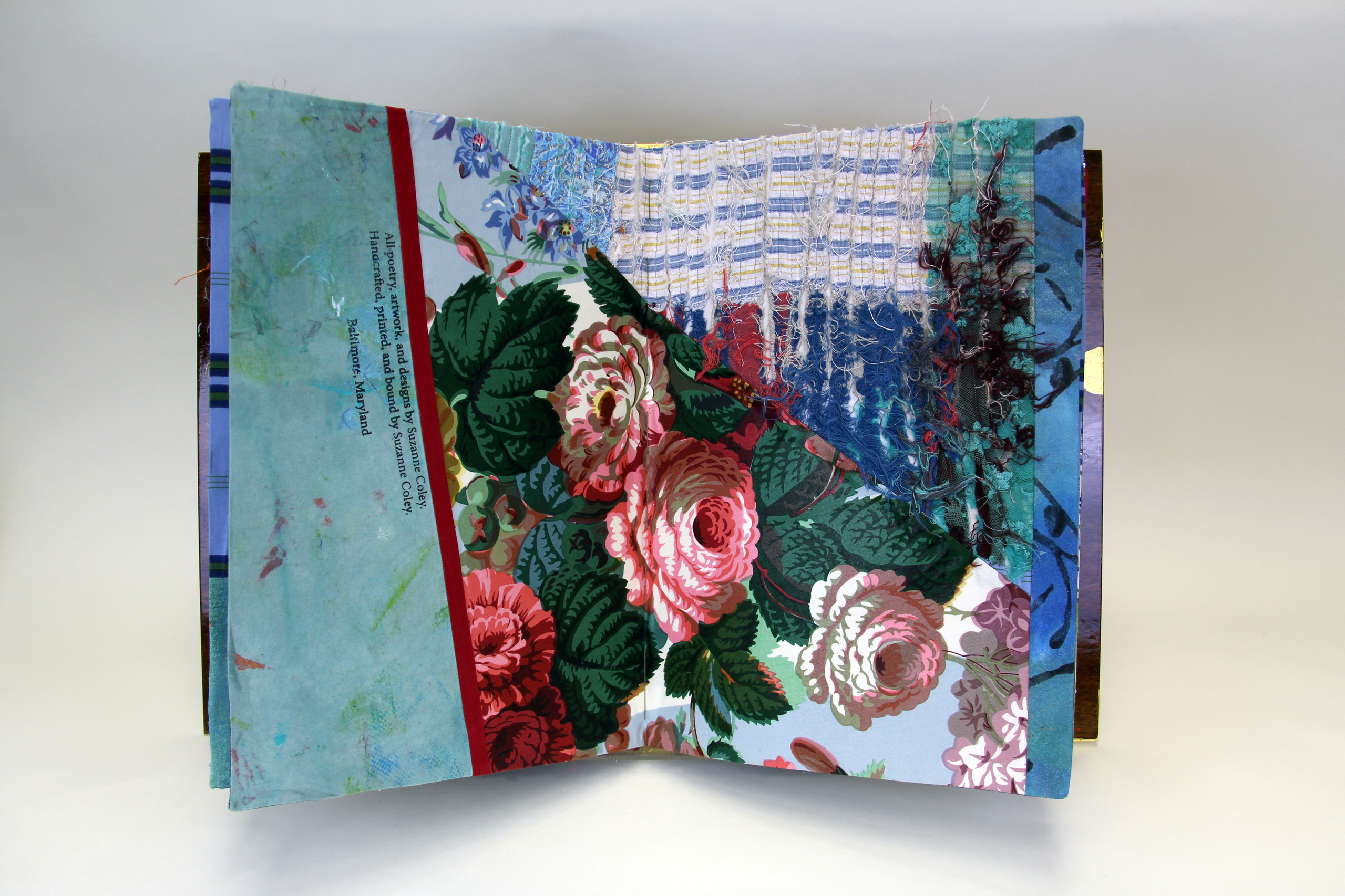 A book made from colorful print fabrics collaged and stitched together is laid flat and open to a spread that features a vibrant floral print.