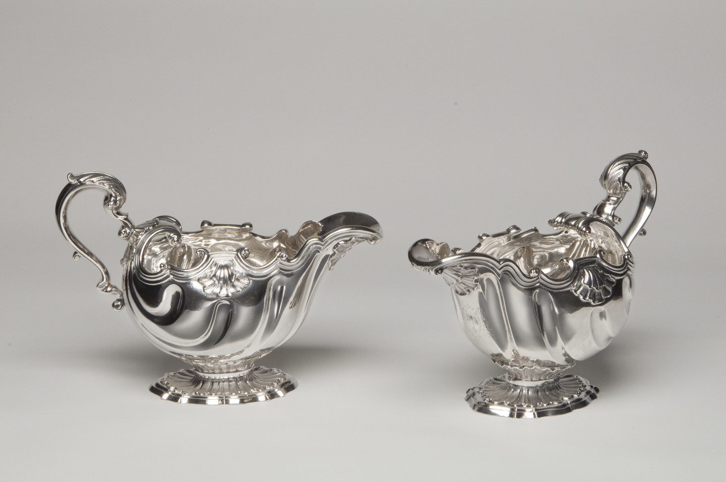 Two silversauce boats decorated with ornate, rococo scrolls, and shells.