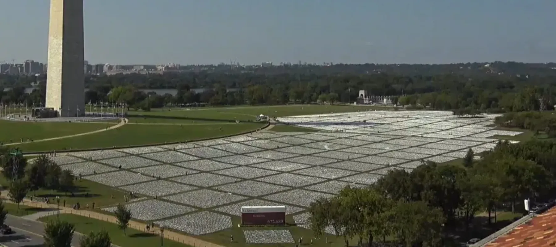 The National Mall with the Washington Monument in the background and thousands of small white flags arrayed across the grassy lawn, seen from above to emphasize their vast number.