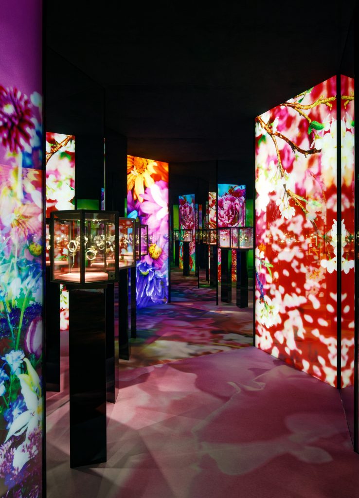 A contemporary, immersive installation features tall, vertical screens that show colorful, closeup views of flowers and botanical patterns.