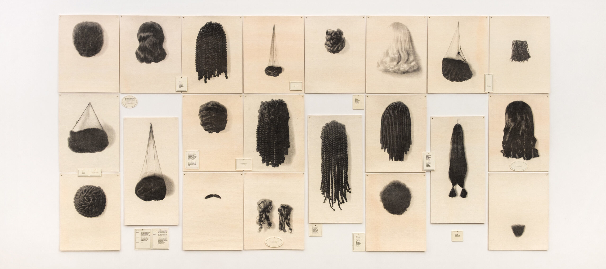 21 off-white, rectangular panels arranged in a large rectangle. A wig is pinned on each panel, and each wig is styled differently, showcasing waves, curls, braids, dreadlocks, and more. All of the wigs are dark-colored, except for one platinum blonde wig at the top.