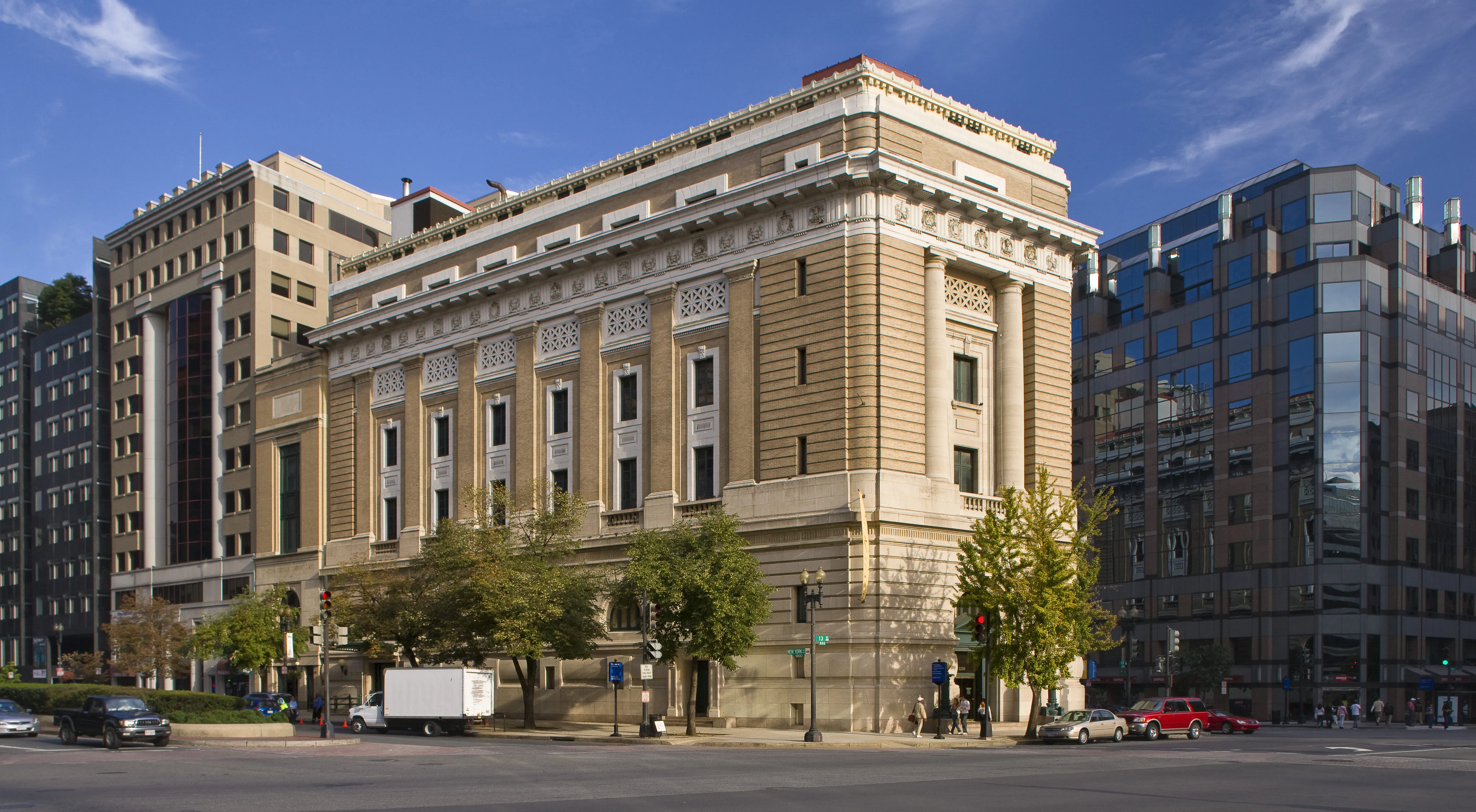 View of the museum from outside showing the Neoclassical building from one corner. The building is a tan-colored stone with an arched doorway, long vertical windows, and detailed molding around the roof.