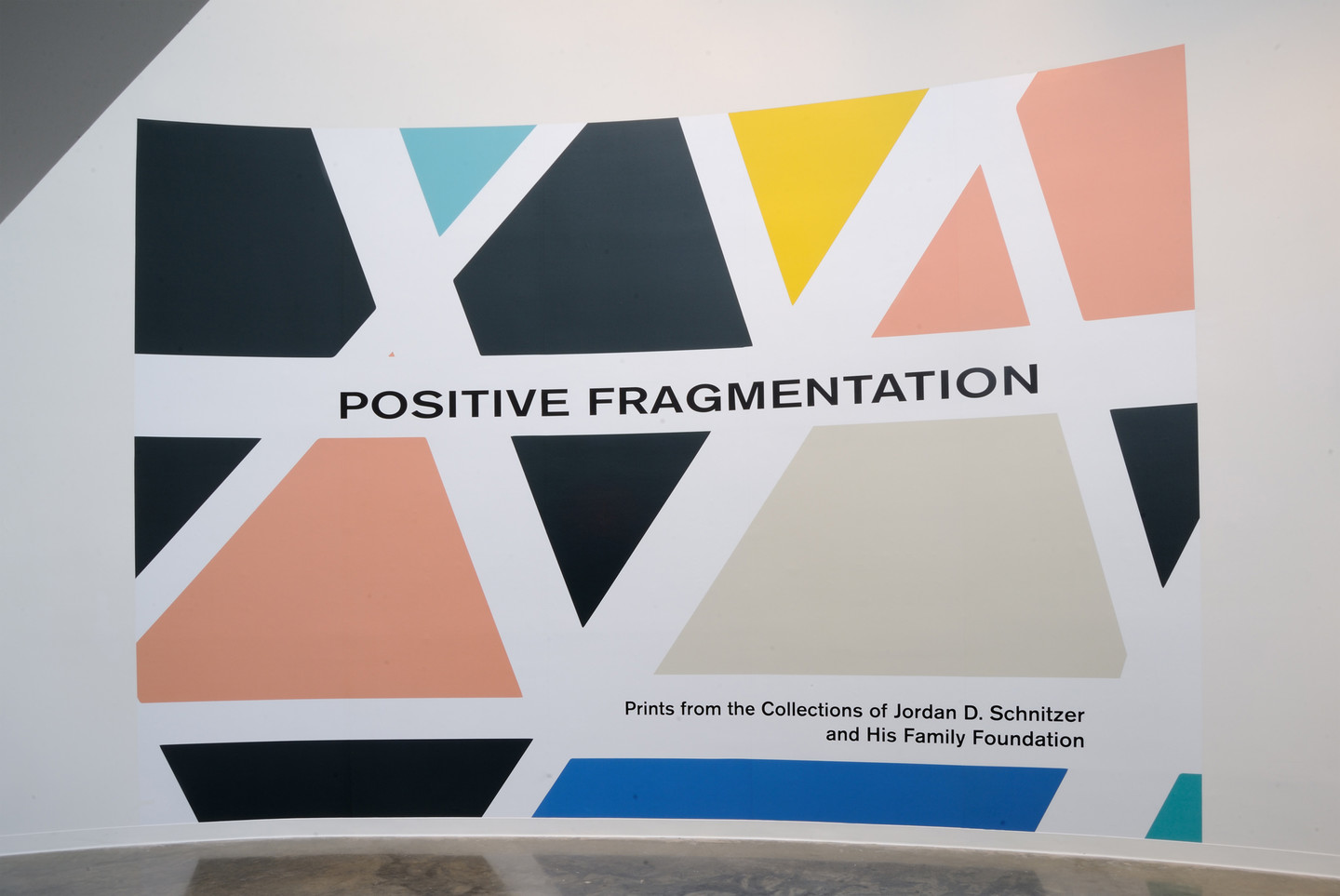 A curved white wall with a colorful geometric wall decal that reads "Positive Fragmentation" and "Prints from the Collections of Jordan D. Schnitzer and His Family Foundation"