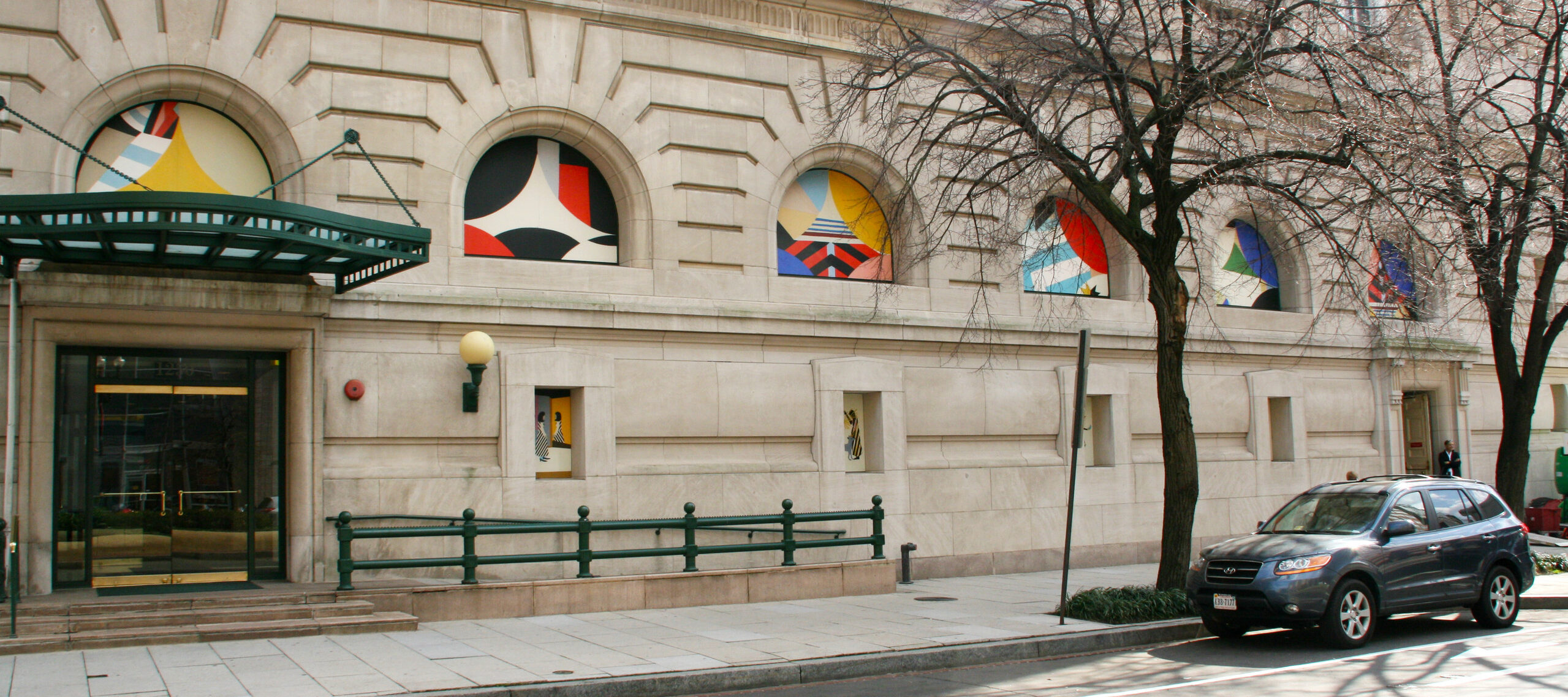 The exterior of the National Museum of Women in the Arts, showcasing colorful, geometric artworks in arched windows set into a classical, tan-colored building.