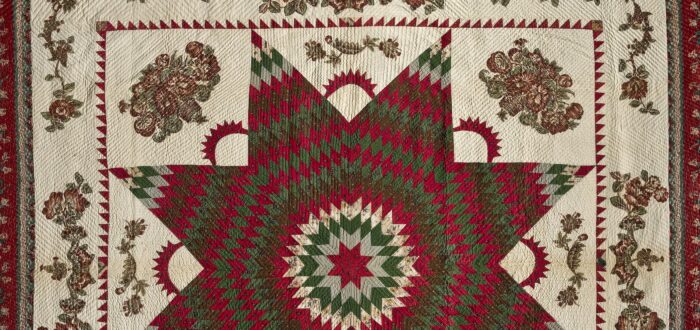 Vintage quilt in dark reds and greens on a cream background. In the center is a large eight-point Star of Bethlehem surrounded by Victorian floral appliques. The border, edged in dark red fabric, features matching floral garland appliques.