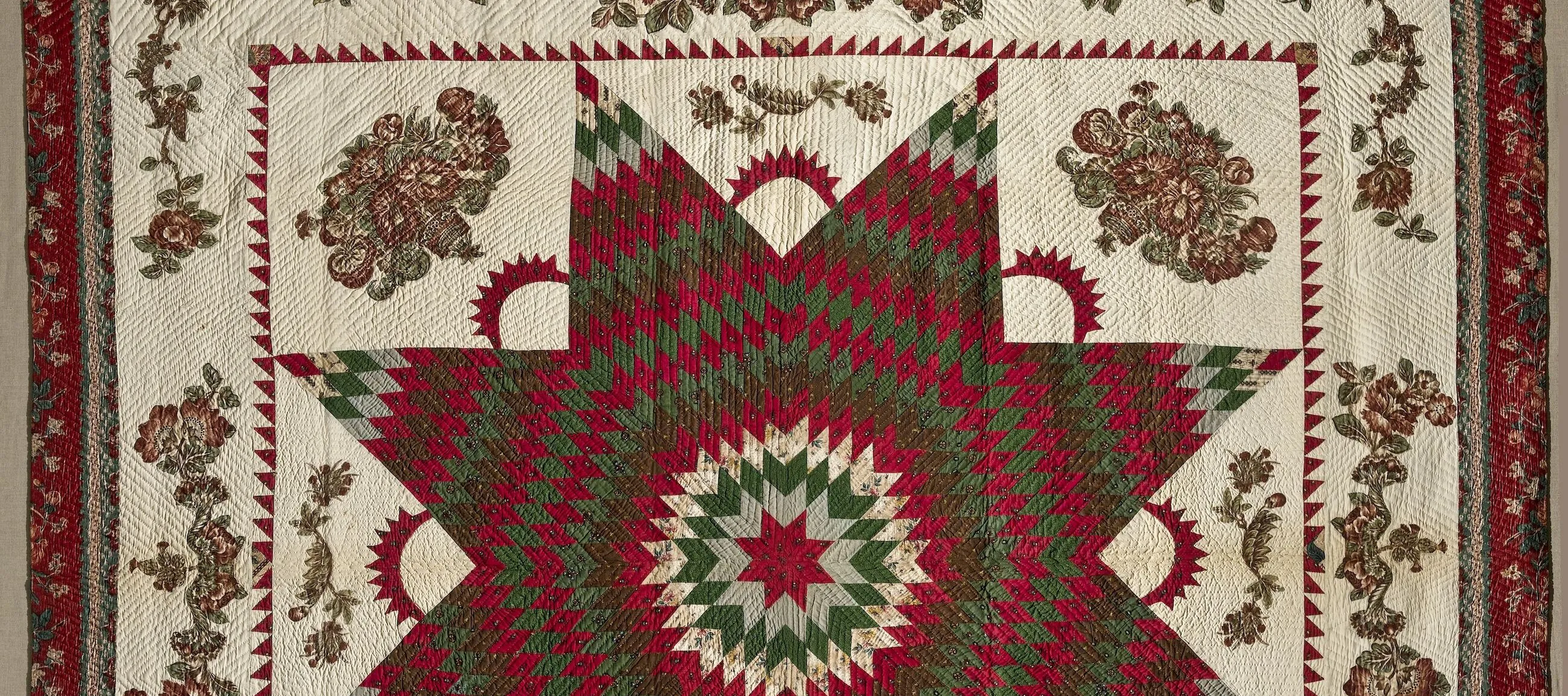 Vintage quilt in dark reds and greens on a cream background. In the center is a large eight-point Star of Bethlehem surrounded by Victorian floral appliques. The border, edged in dark red fabric, features matching floral garland appliques.