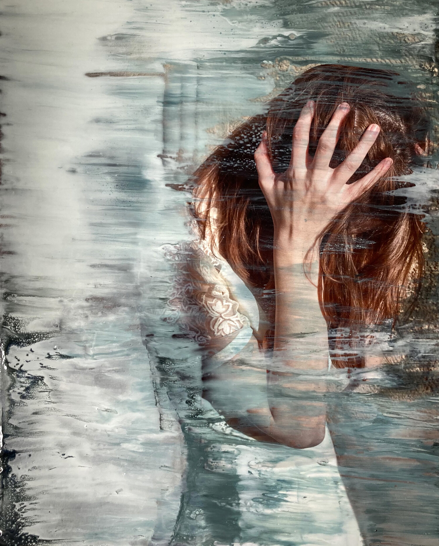 A photograph of a light skinned woman with red hair wearing a white dress. The figure has her head bent down with her hair in her face and her hands holding either side of her head. There are semi-translucent white and teal brush strokes over part of the image.