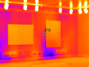 A thermal imaging photograph of a museum gallery wall. The coloring shows heat represented in orange, and heat loss/cold represented in purple, which takes up the areas below, above, and around two paintings.