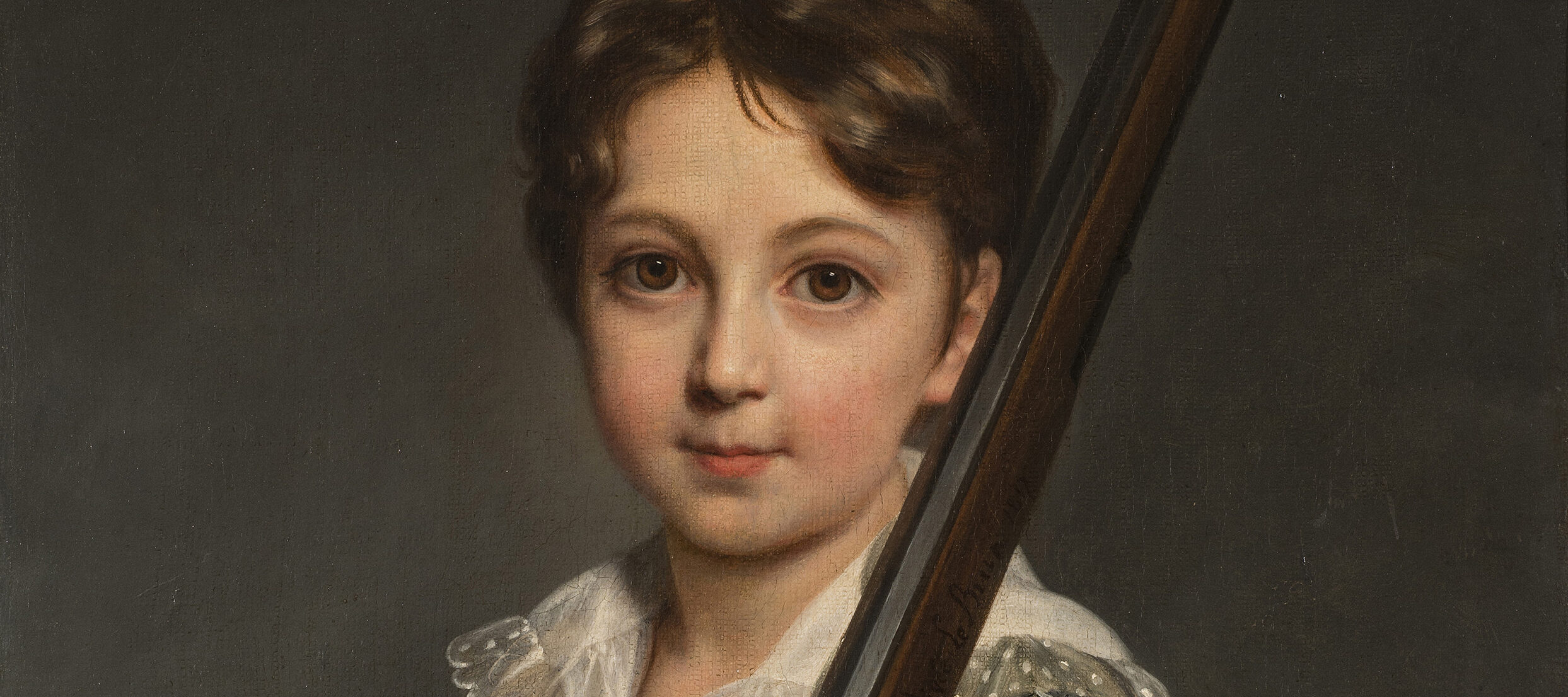 A young boy with light skin and brown hair faces the viewer while cradling the stock of a rifle in his arms and resting the barrel on his left shoulder. He wears a delicate lace collar and is shown against a gray background with visible brushstrokes.
