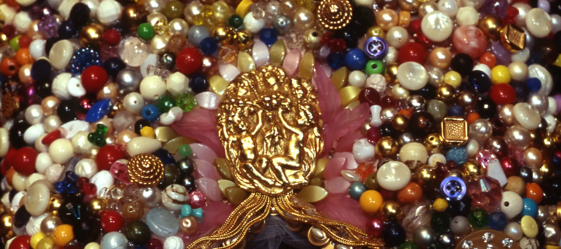 Colorful beading with a gold medallion in the center, featuring two nude, sculpted figures sitting with their arms raised.