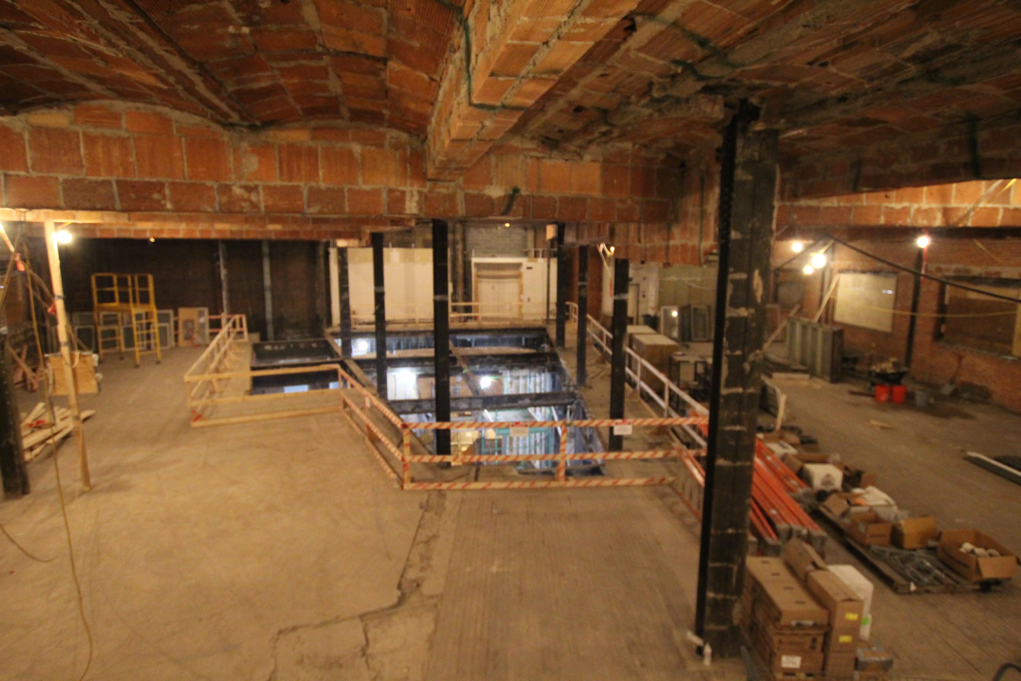 Interior of museum's 4th floor demo with exposed brick, bare floors, metal supports, a large reinforced hole in the middle of the floor.