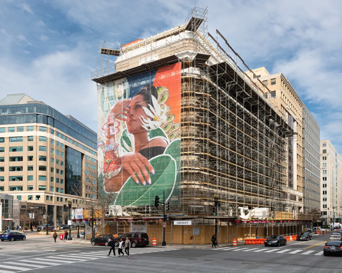 A colorful mural of a woman with flora on scaffolding on the museum building.