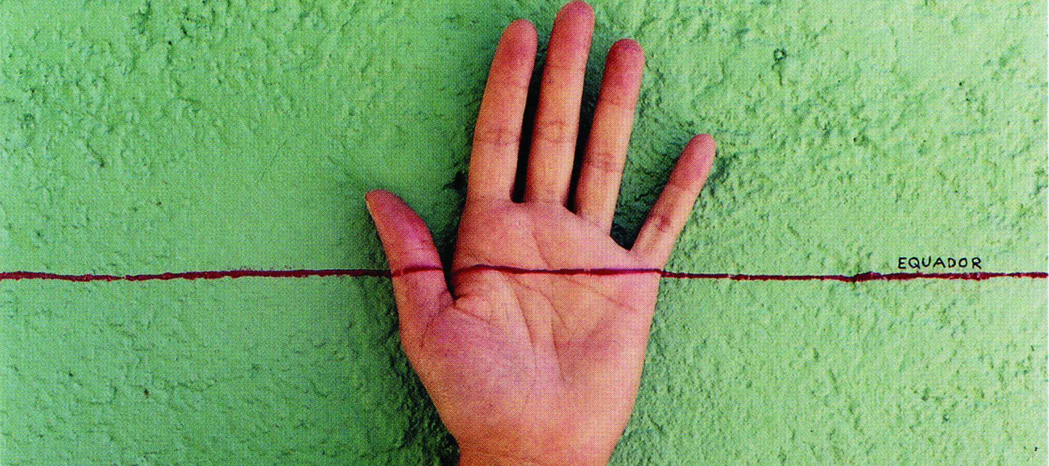 A light-skinned, left hand facing palm-out against a mottled, green-gray wall. A horizontal red line is drawn across the middle of the composition and the middle of the hand. On top of the red line on the right, is the word ‘EQUADOR’ written in small, black, capital letters.