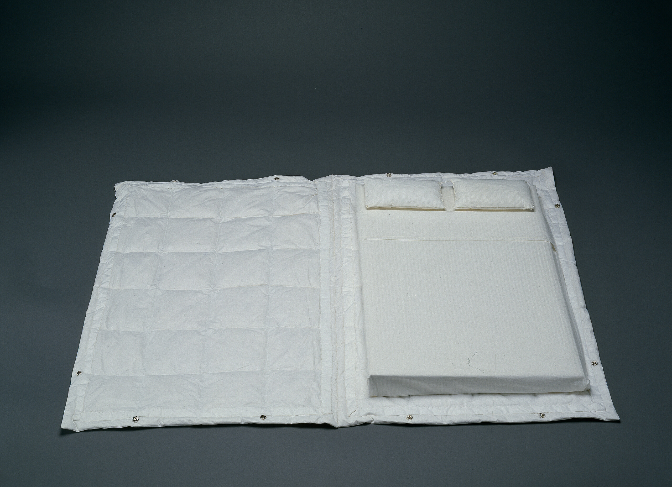A open book with a cover made out of a white comforter and pages in the shape of a mattress covered in white sheets with two white pillows at the top.