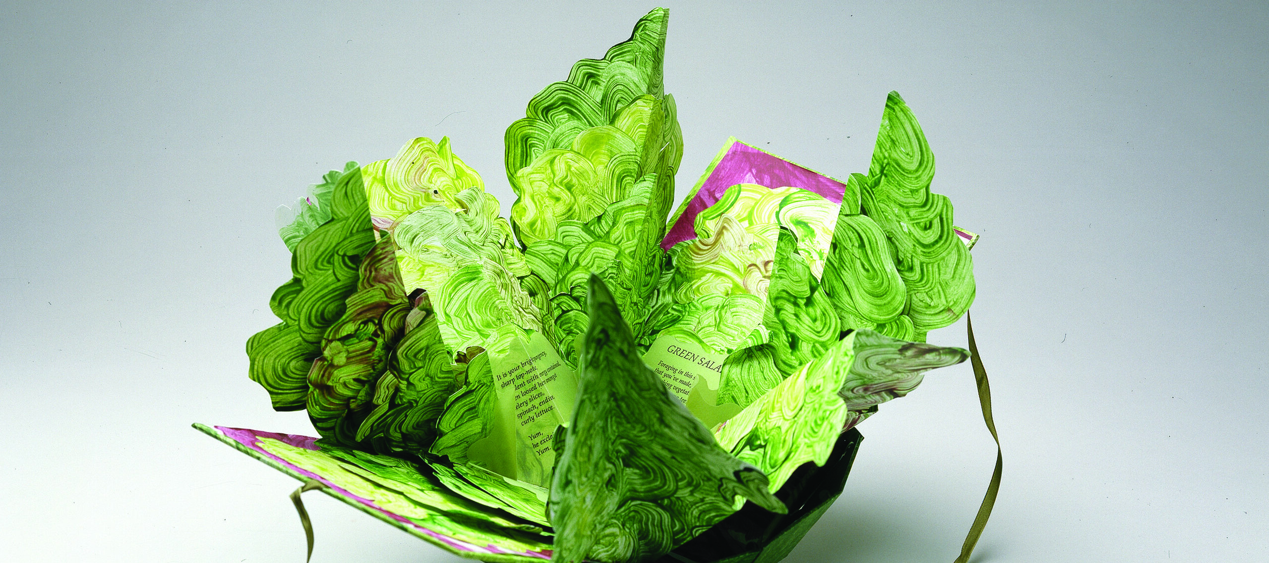 Artist's book resembling a salad in a bowl. Constructed of Tyvek that has been painted in swirling greens and map-folded to look like leaves of lettuce, there is poem written on the inner the leaves.