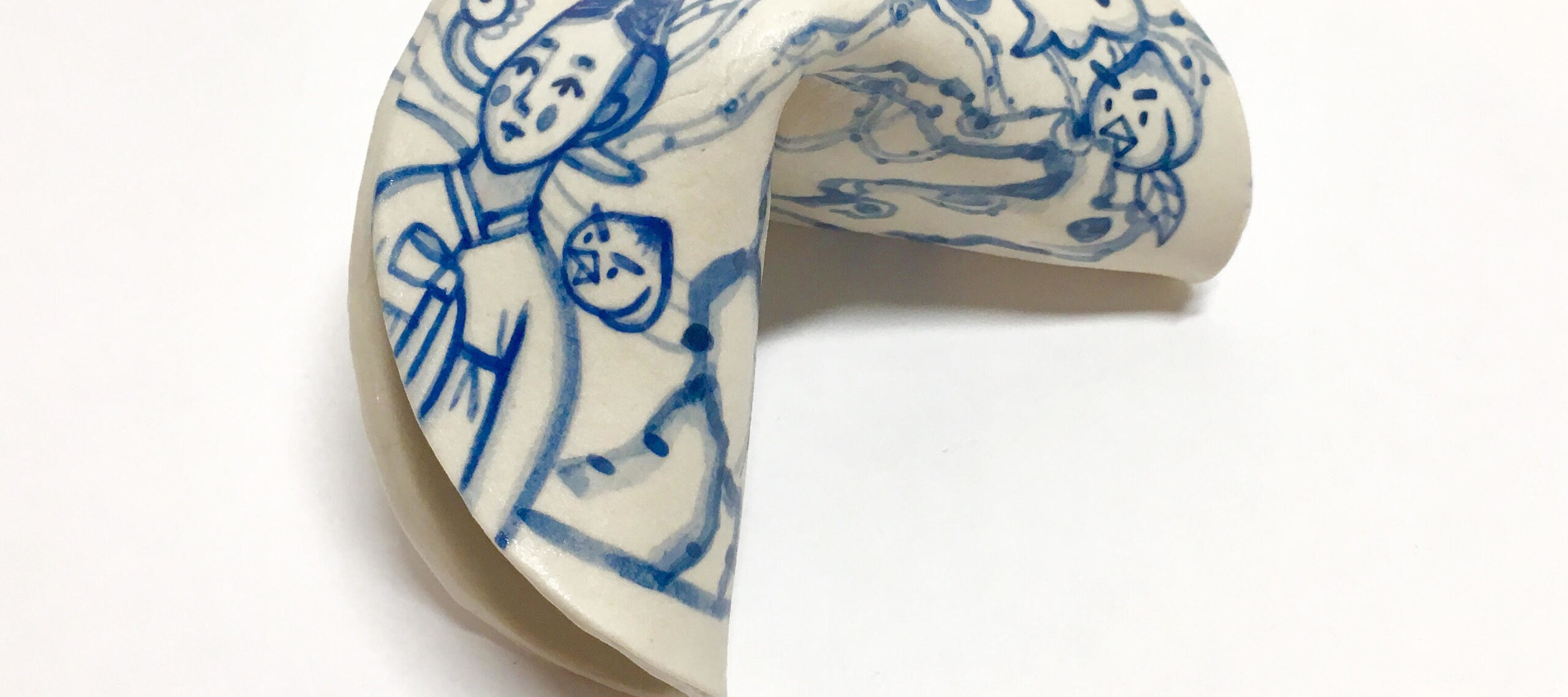 A blue and white painted porcelain fortune cookie depicting a woman in a hanbok standing in a garden of tall trees dotted with large peaches with faces and beaks on them. On the cookie’s edge is a red stamp with the artist’s name.