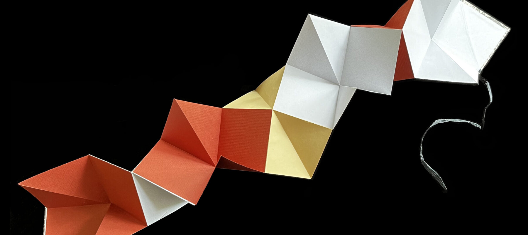 Linked petal-fold book that opens lengthwise and is made of folded alternating squares of yellow, orange, and white paper. Covers and strings to bind the book are visible on the right and left end pages.
