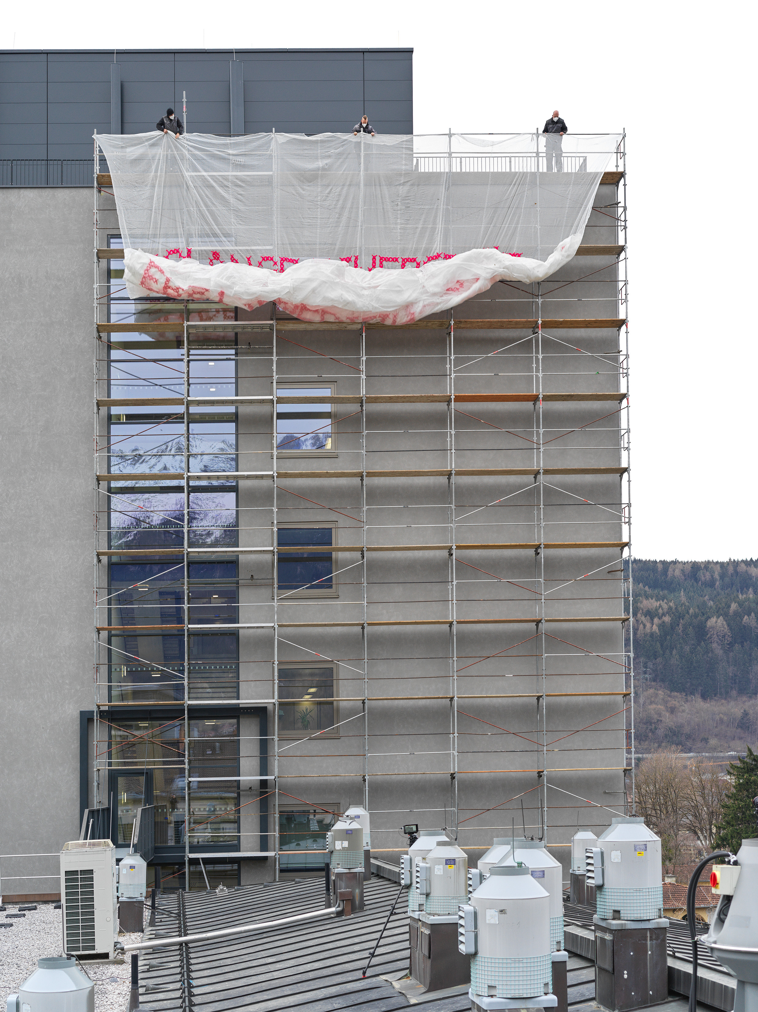 White mesh scrim is unfurled from the top of a building to cover several floors of scaffolding.