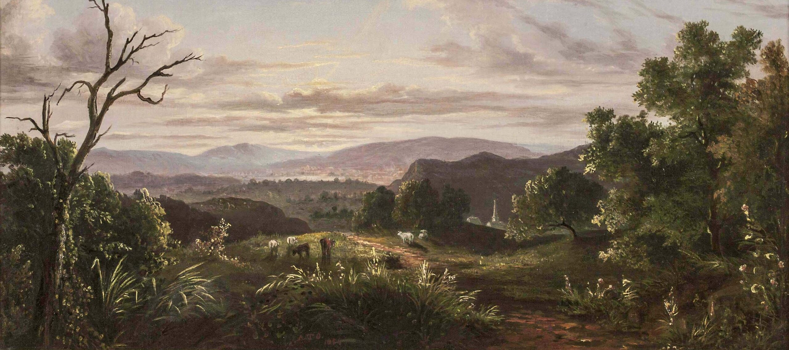 Livestock graze along a path cutting through a vast landscape of green, rolling hills covered in trees. The path leads into the mountainous distance, where more foliage and a few building tops are visible. The expansive, pale blue sky is tinged with pink and purple, with white clouds.