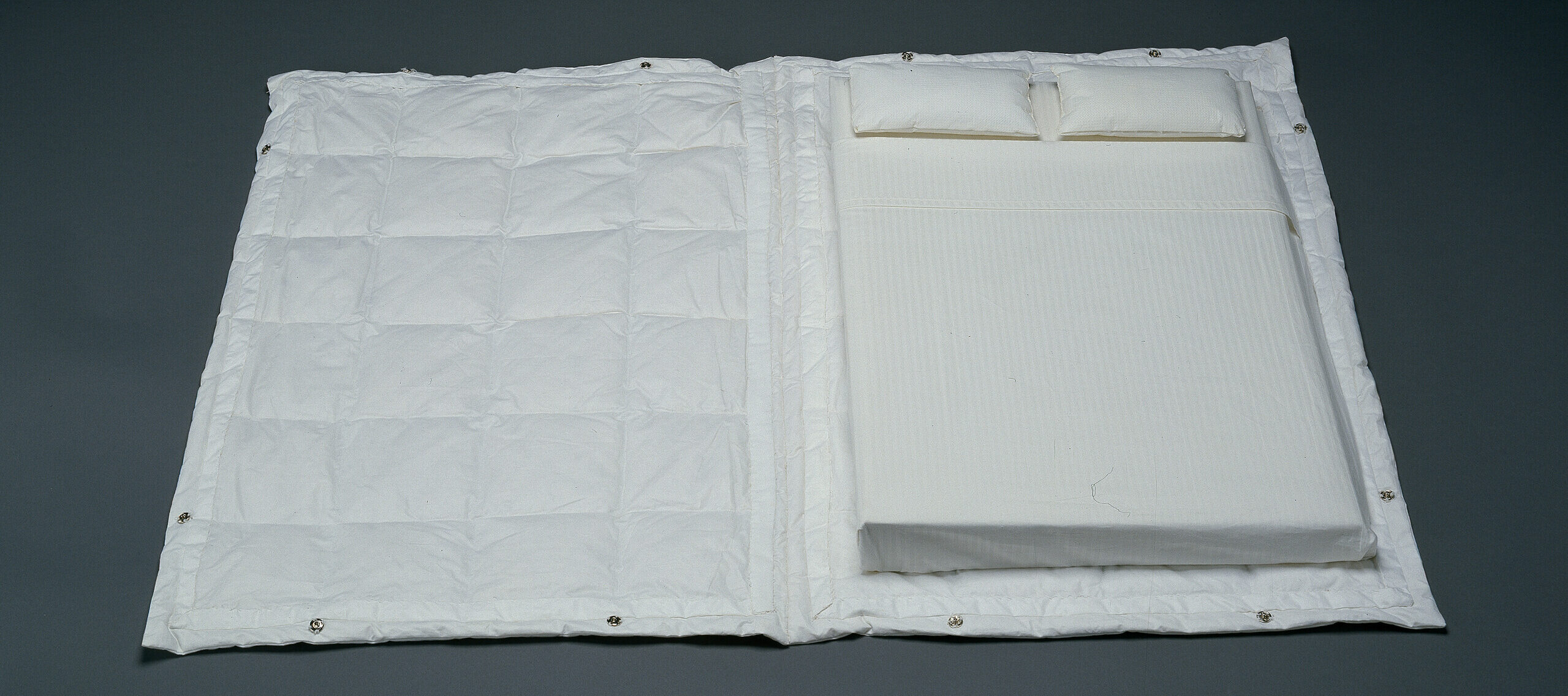 A open book with a cover made out of a white comforter and pages in the shape of a mattress covered in white sheets with two white pillows at the top.