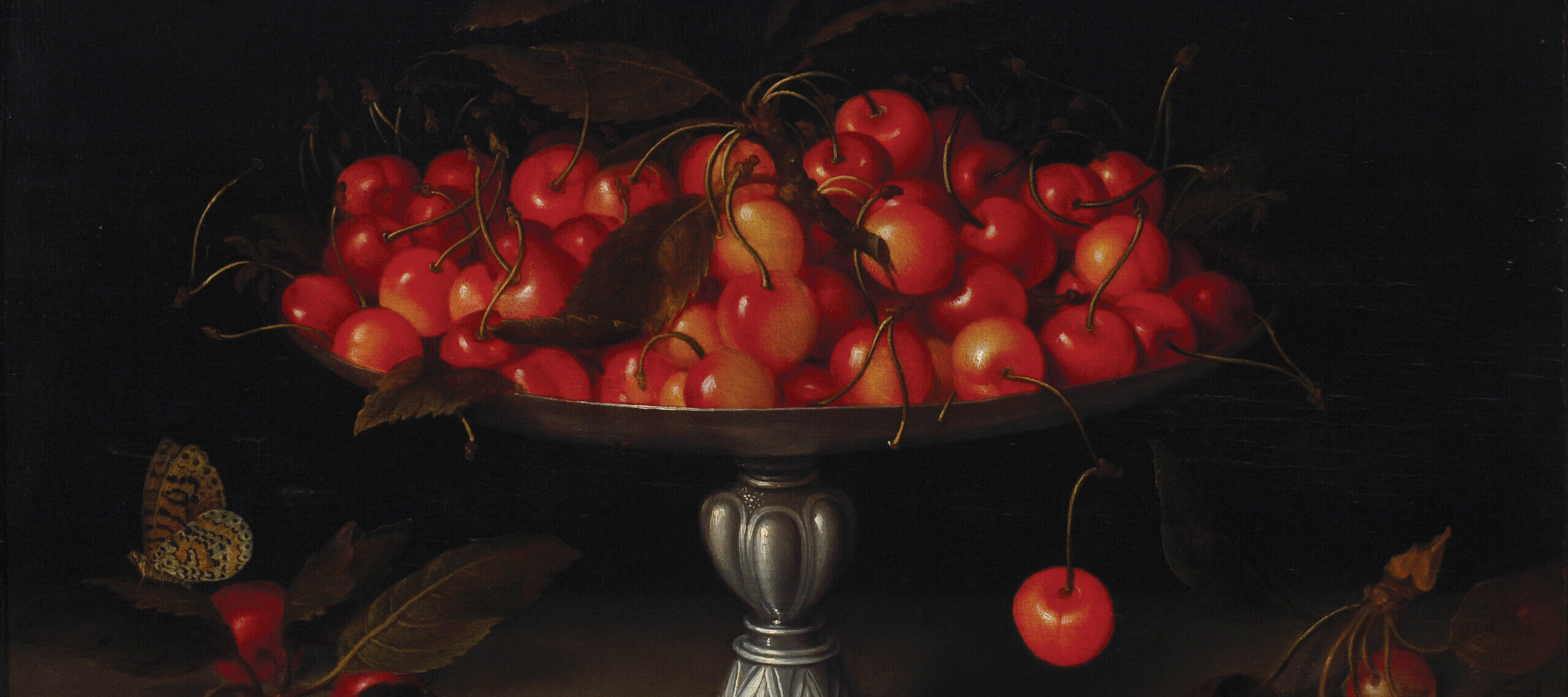 An opulent, footed silver bowl overflows with ripe cherries in front of a dramatic dark background. Additional fruits lie on the table below the bowl, and a butterfly flutters to one side.