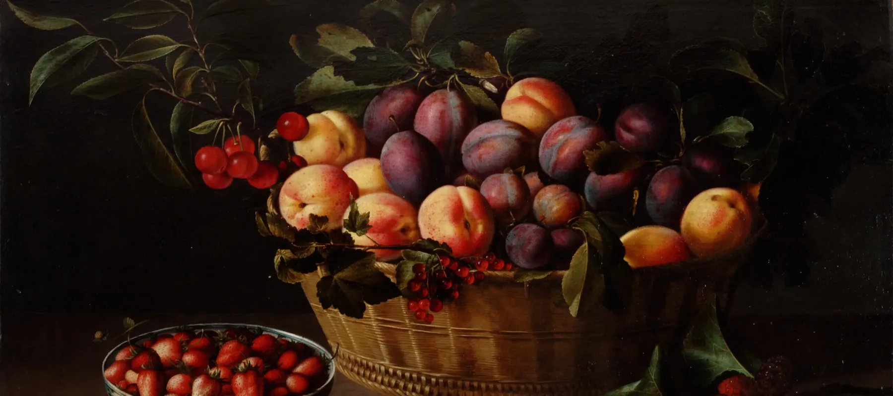 A brightly lit basket of peaches and plums on a ledge against a dark background. To the left of the basket is a blue and white porcelain bowl filled with strawberries. A whole fig sits next to it. In front of the basket is half of a fig and to the right a branch with leaves and red berries.