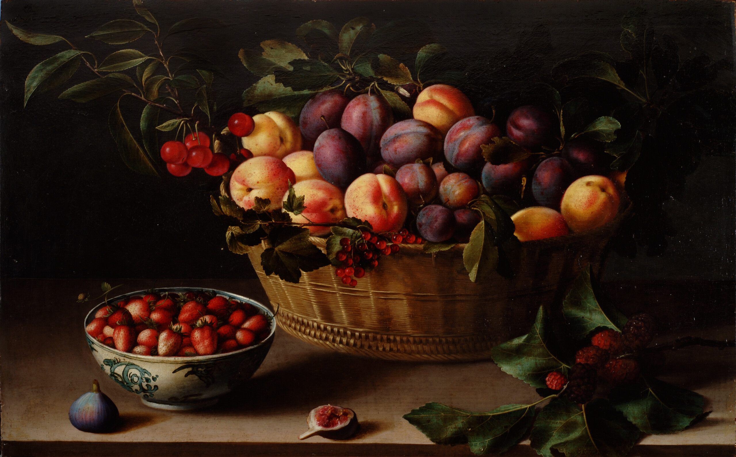 A brightly lit basket of peaches and plums on a ledge against a dark background. To the left of the basket is a blue and white porcelain bowl filled with strawberries. A whole fig sits next to it. In front of the basket is half of a fig and to the right a branch with leaves and red berries.