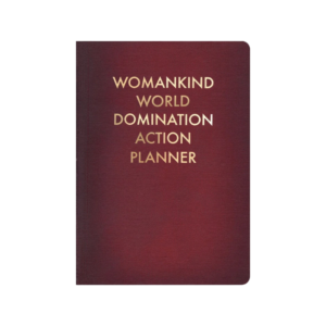 A maroon notebook with gold lettering printed on the cover that says Womankind World Domination Action Planner. 