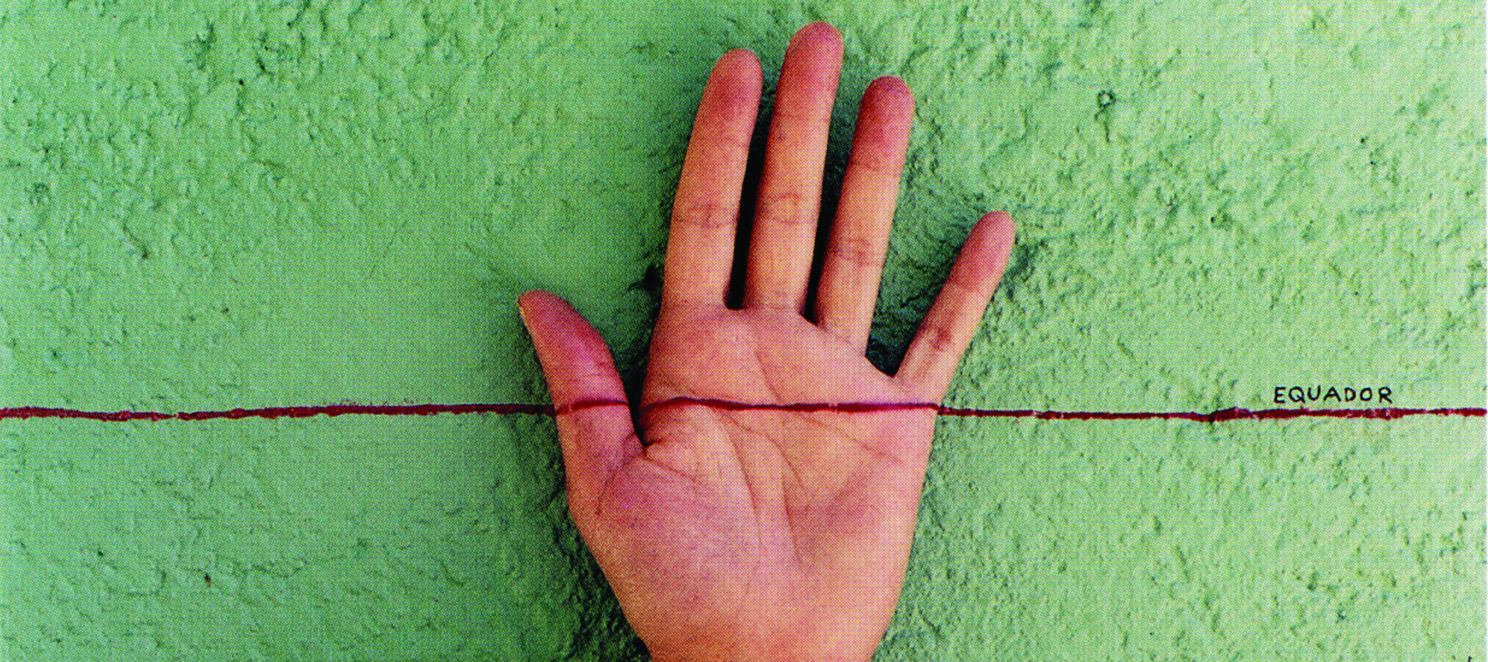 A light-skinned, left hand facing palm-out against a mottled, green-gray wall. A horizontal red line is drawn across the middle of the composition and the middle of the hand. On top of the red line on the right, is the word ‘EQUADOR’ written in small, black, capital letters.