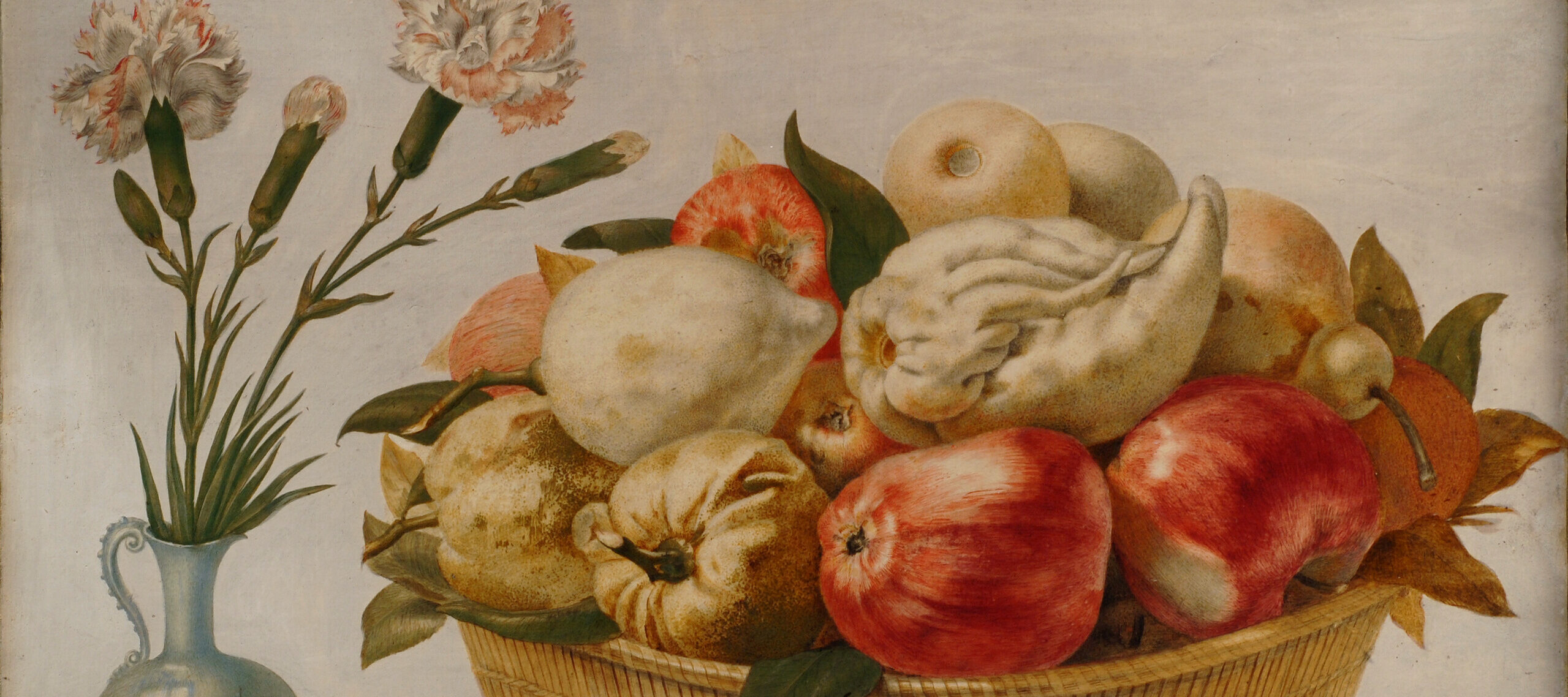 A round, straw basket filled with red apples and pale fruits and vegetables on a stone ledge against a light background. A light blue vase with pink and white carnations sits beside the basket. Two oblong, mottled seashells sit in front of the basket and vase.