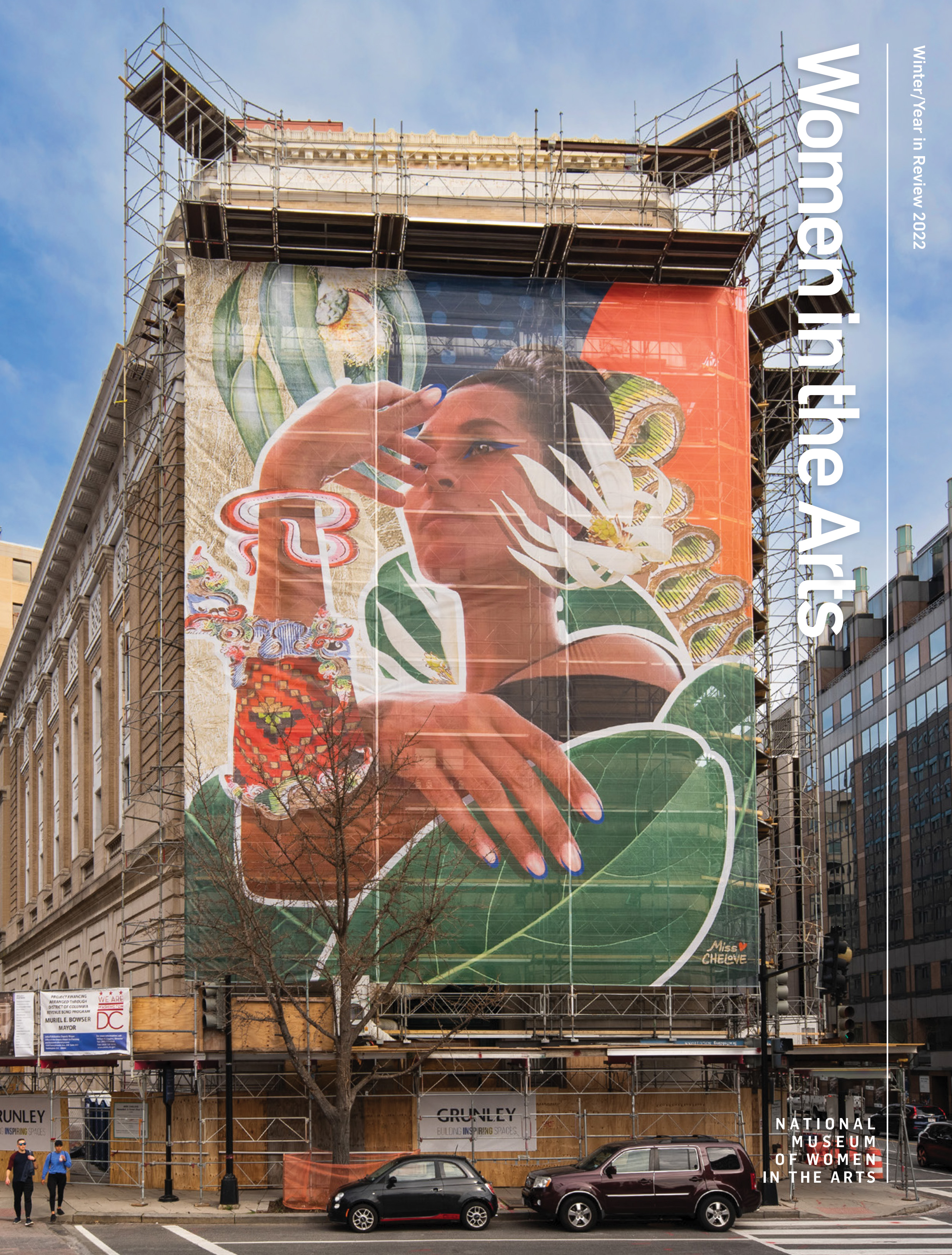 Magazine cover features the exterior view of the museum with scoffolding all around that features a large, colorful mural on the front depicting a dark-skinned woman gazing into the distance with her arm touching her face.