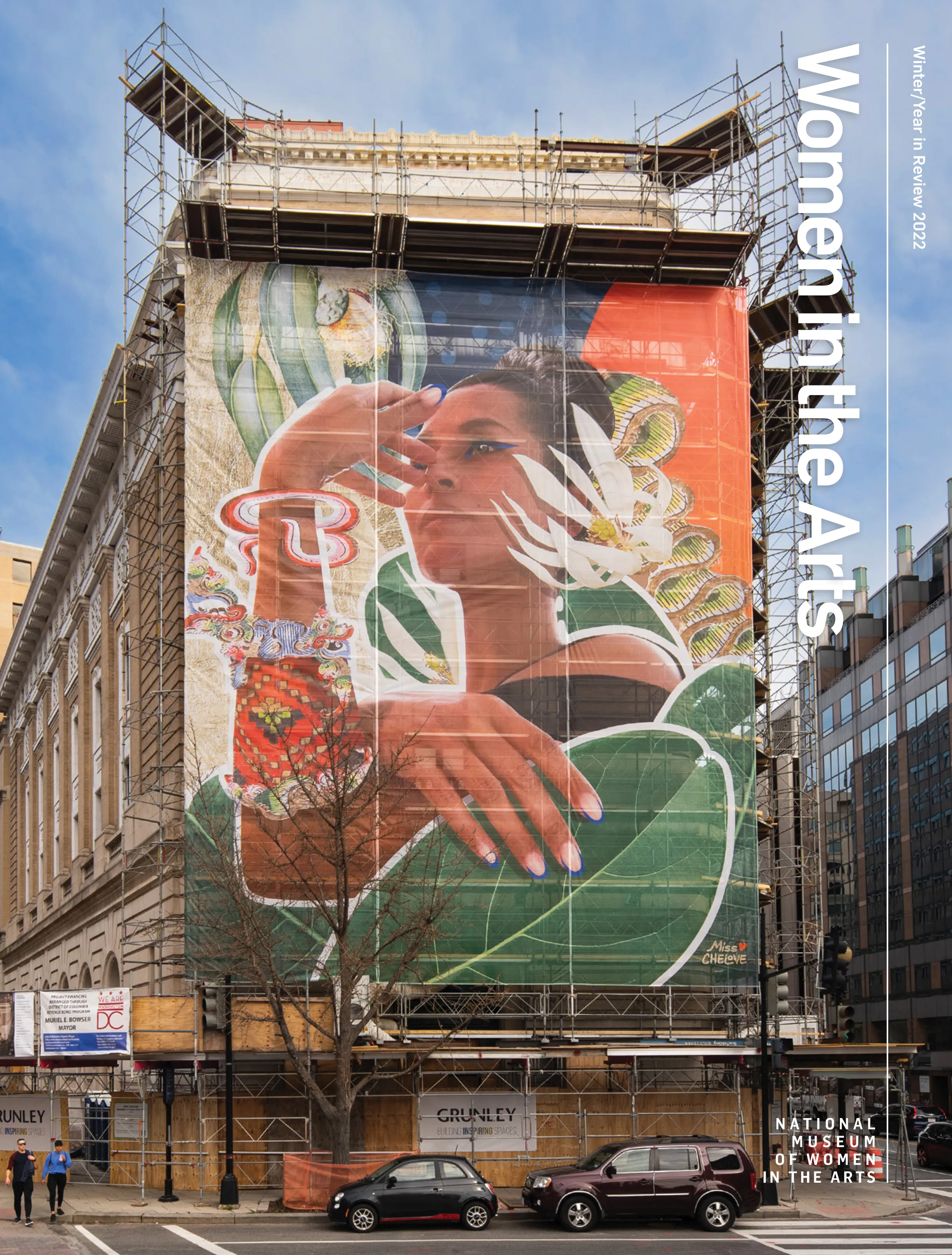 Magazine cover features the exterior view of the museum with scoffolding all around that features a large, colorful mural on the front depicting a dark-skinned woman gazing into the distance with her arm touching her face.