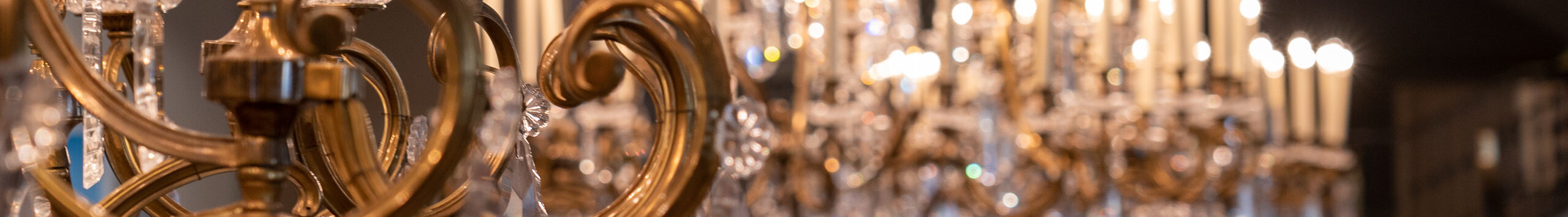 Close-up view of ornate gold and crystal chandeliers in the museum's Great Hall. The camera is focused on the chandelier in the foreground and the rest is out of focus.
